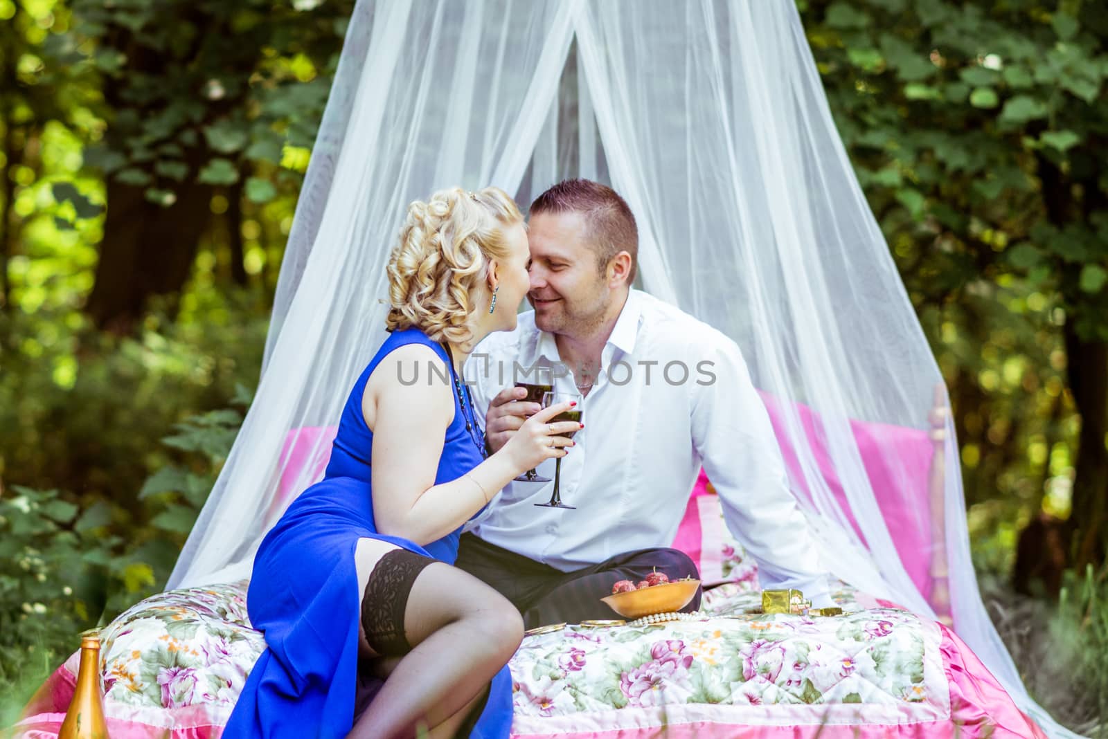 Man and woman sitting on the bed in the lawn and holding a glasses of wine and look at each other in Lviv, Ukraine.