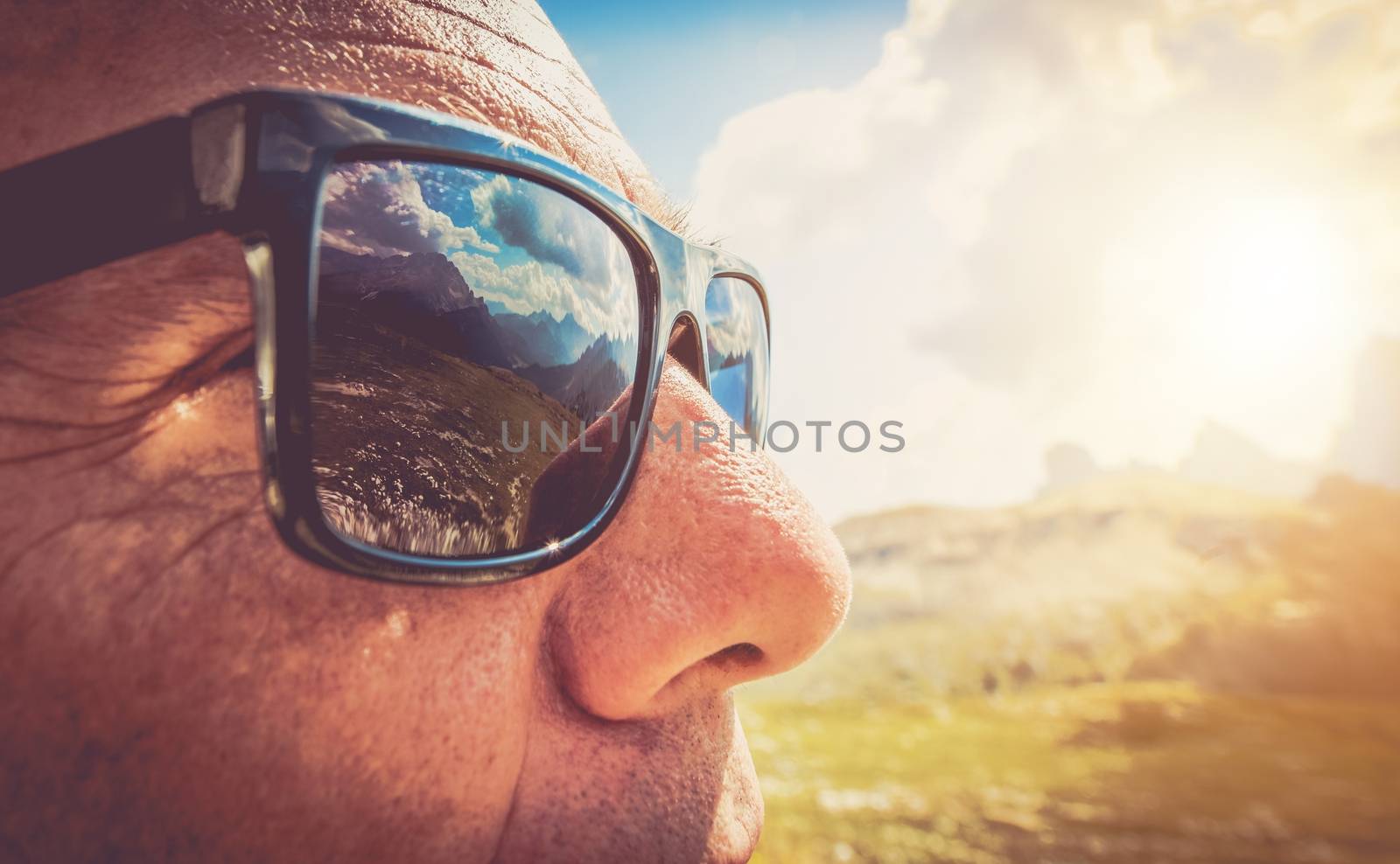 Sunglasses Protection. Caucasian Men in His 50s in the Trendy Black Sunglasses. Closeup Photo. Mountains Reflection in the Lenses.