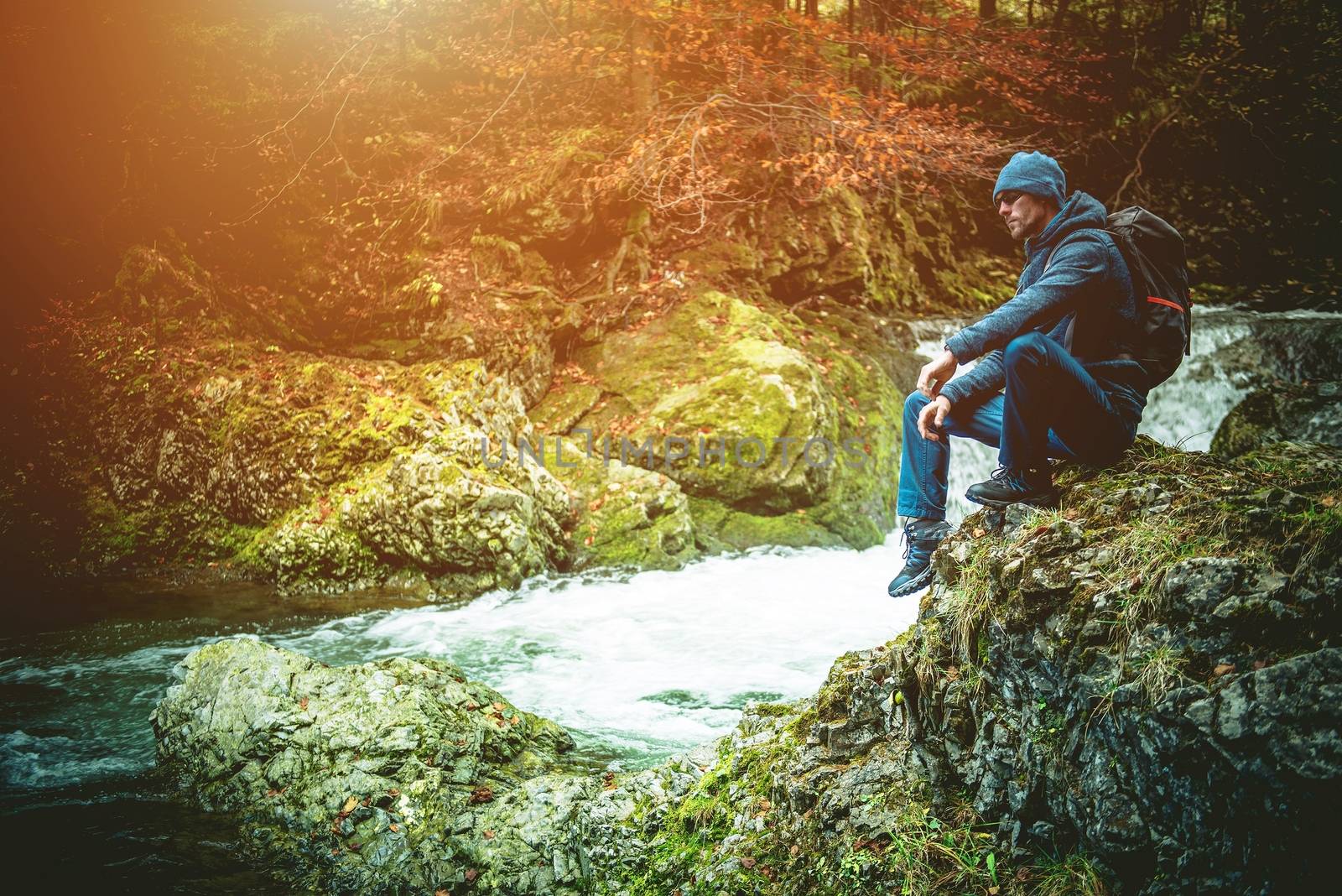 Young Caucasian Hiker on the Mountain Trail Resting on the Large Mountain River Boulder.