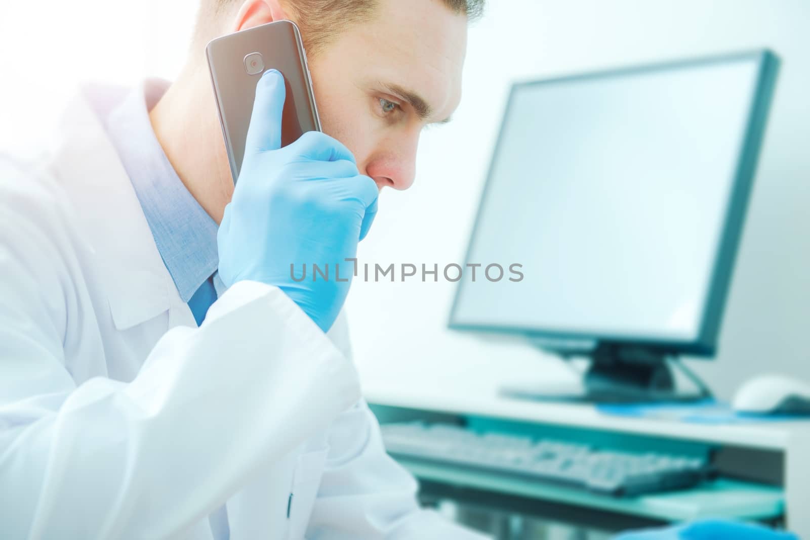 Doctor Phone Call Consultation. Medical Doctor Using His Phone and Computer To Get Second Opinion. Mid 30s Caucasian Doctor.