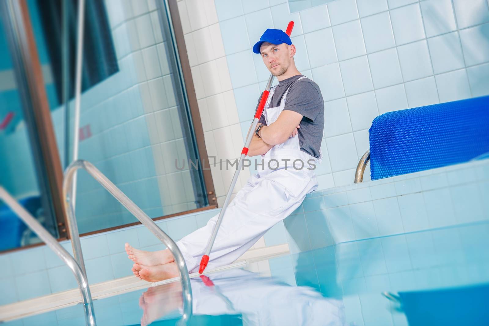 Swimming Pool Technician Cleaner Taking Rest Break On the Edge of Large Indoor Pool.