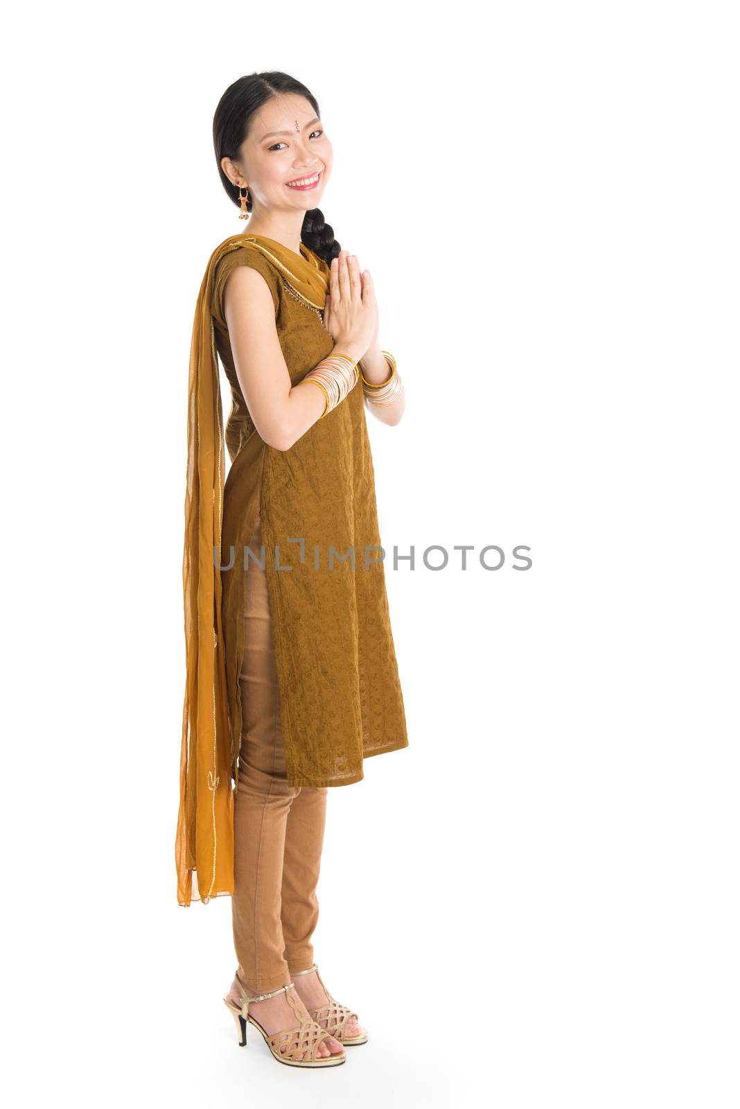 Young mixed race Indian Chinese girl in traditional punjabi dress greeting, full length standing isolated on white background.