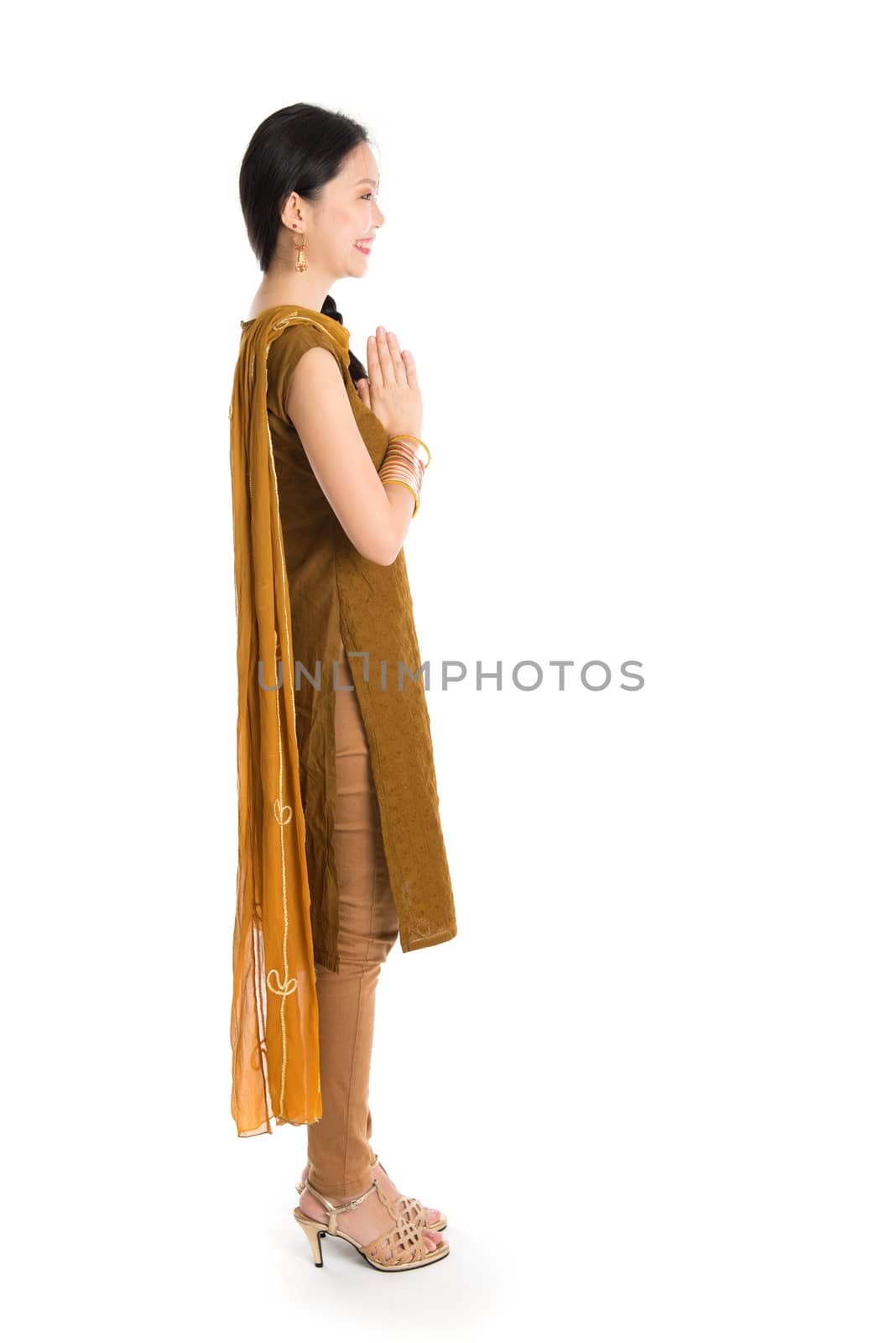 Side view of young mixed race Indian Chinese girl in traditional punjabi dress greeting, full length standing isolated on white background.