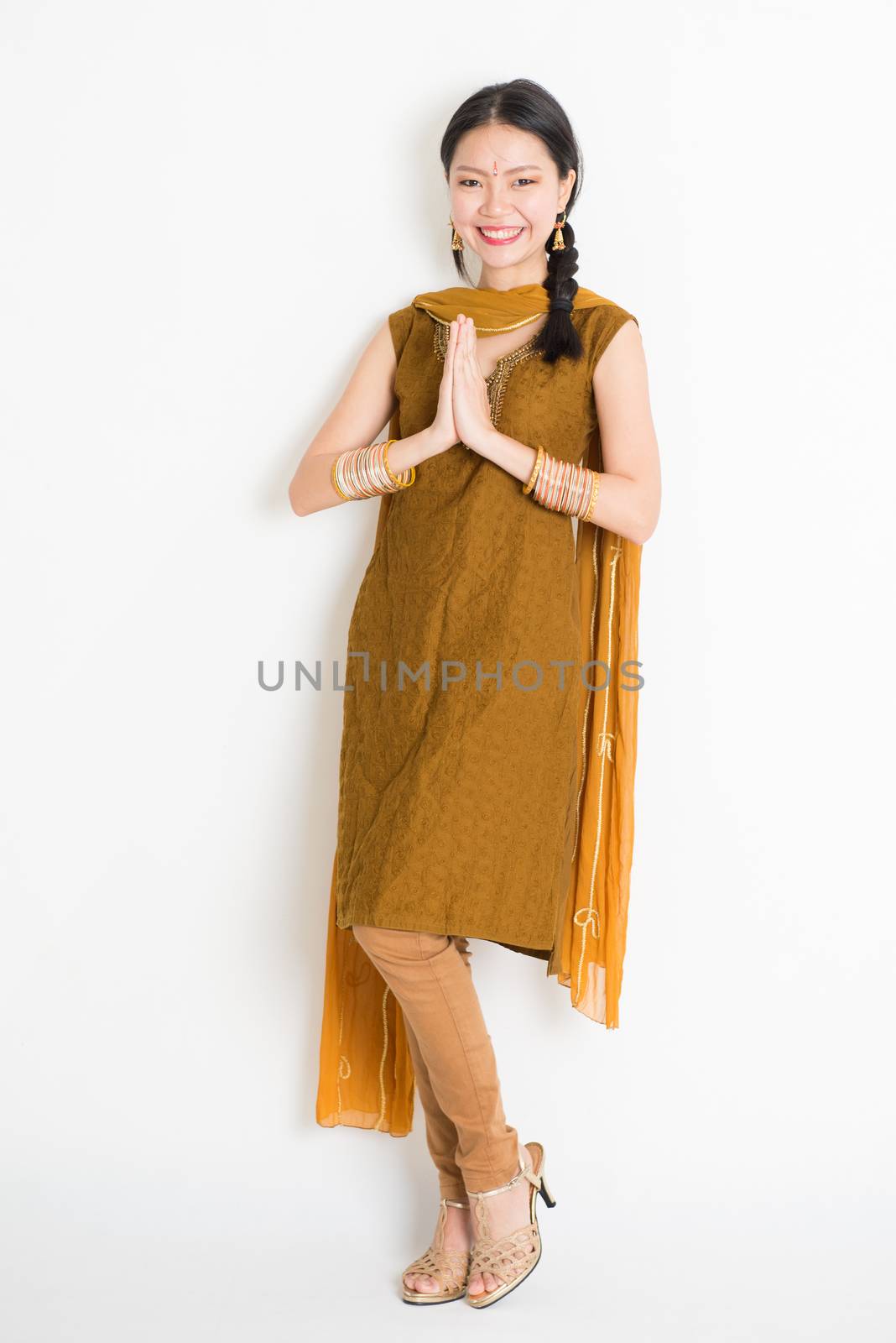 Portrait of mixed race Indian Chinese girl in traditional punjabi dress greeting, full length standing on plain white background.