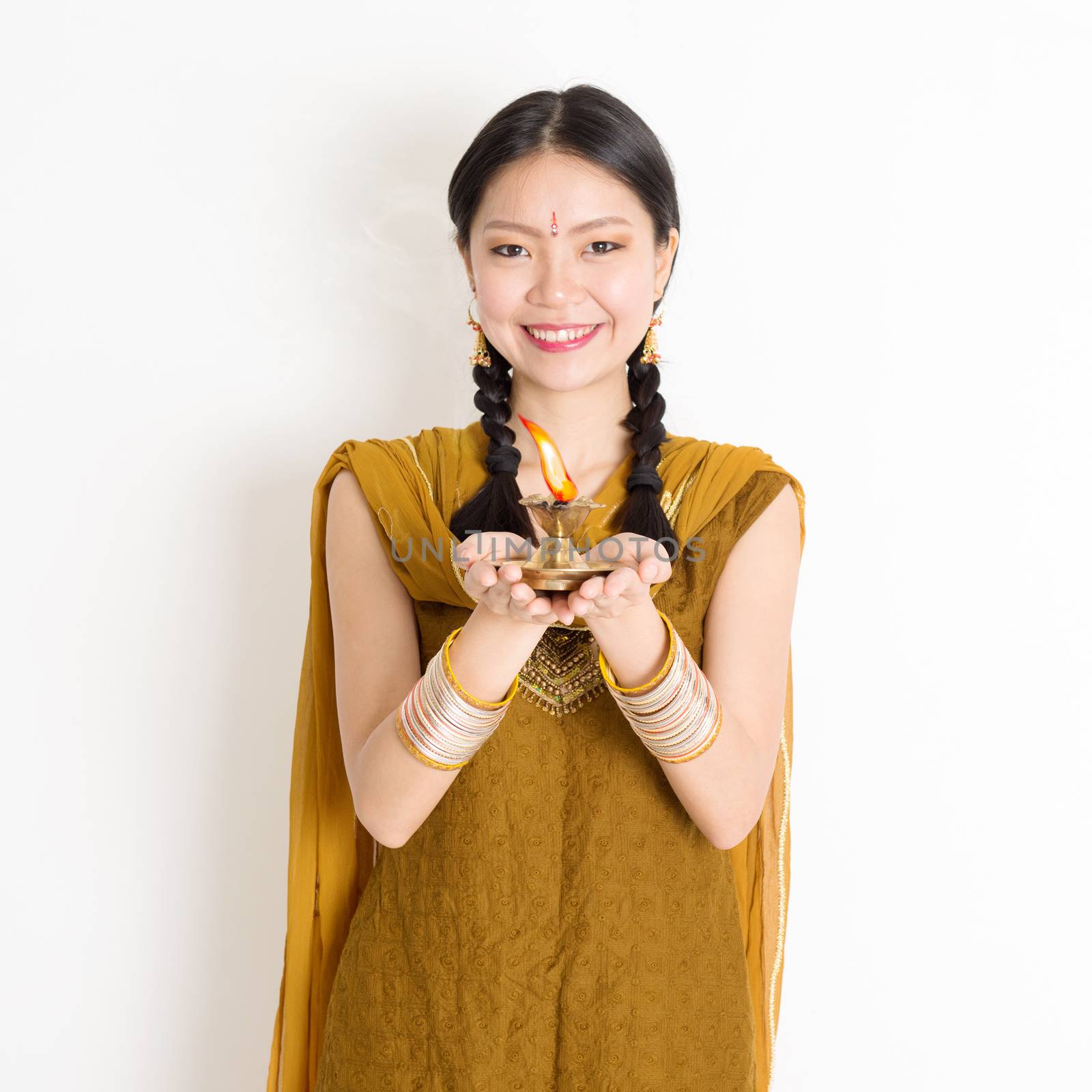 Mixed race Indian Chinese girl in traditional dress hands holding diya oil lamp and celebrating Diwali or deepavali, fesitval of lights.