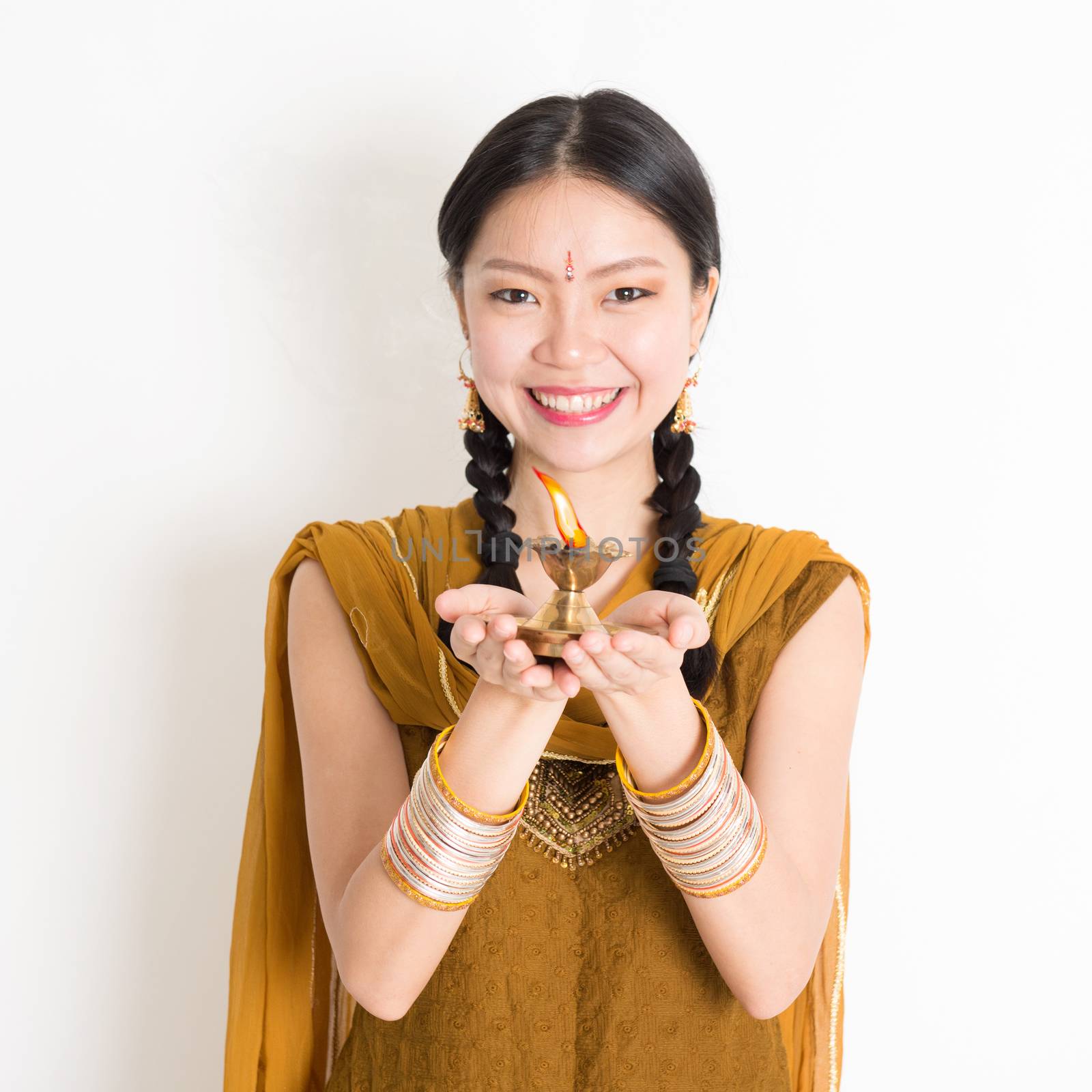 Mixed race Indian Chinese female in traditional dress hands holding diya oil lamp and celebrating Diwali or deepavali, fesitval of lights.