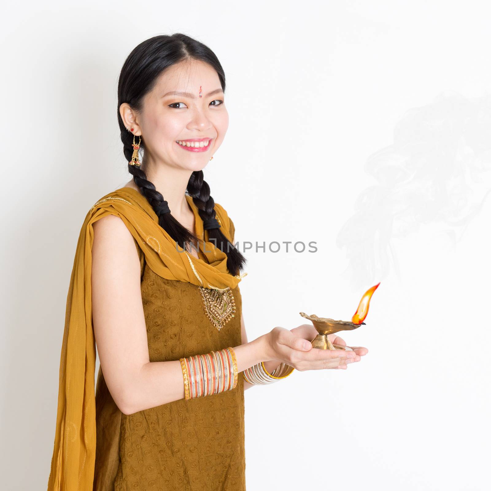 Mixed race Indian Chinese girl in traditional dress hands holding diya oil lamp and celebrating Diwali or deepavali, fesitval of lights.