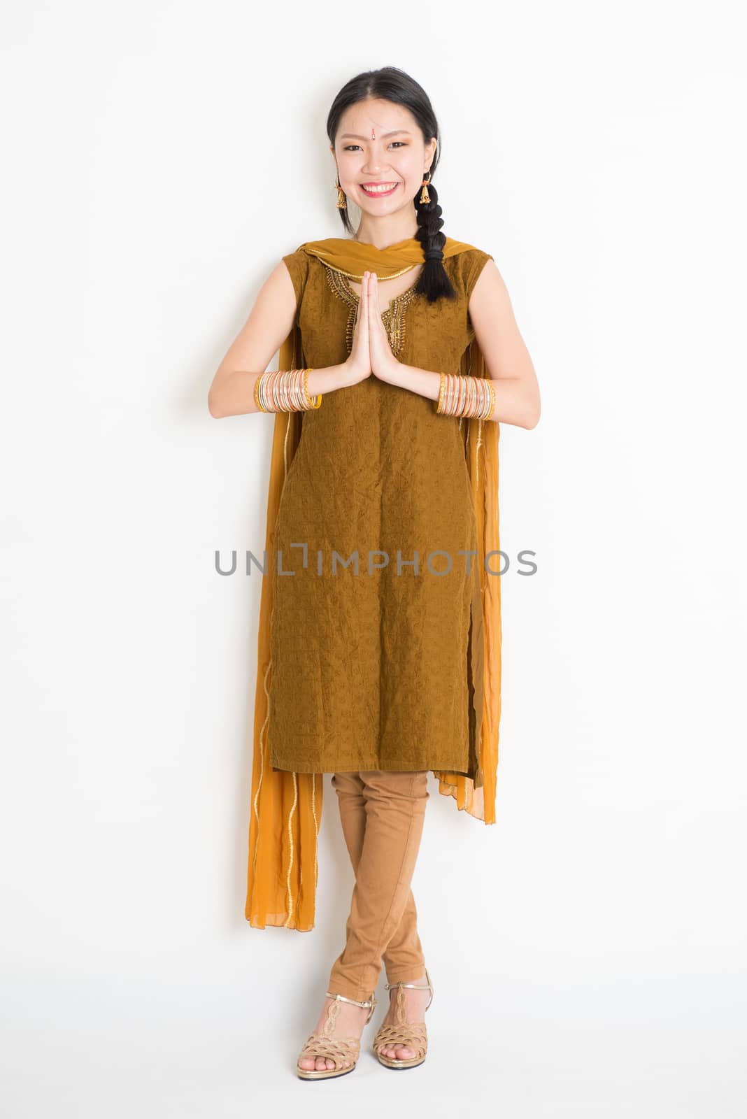 Portrait of mixed race Indian Chinese woman in traditional punjabi dress greeting, full length standing on plain white background.