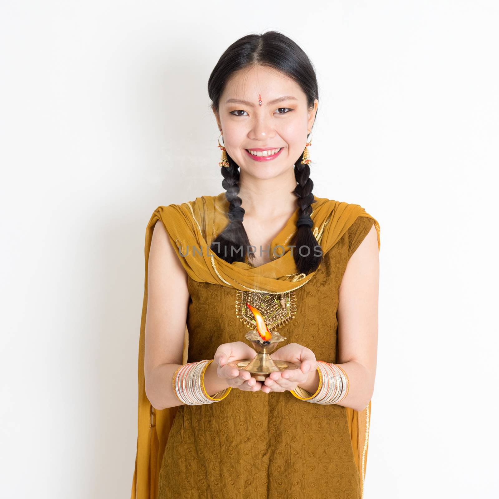 Mixed race Indian Chinese woman in traditional dress hands holding diya oil lamp and celebrating Diwali or deepavali, fesitval of lights.