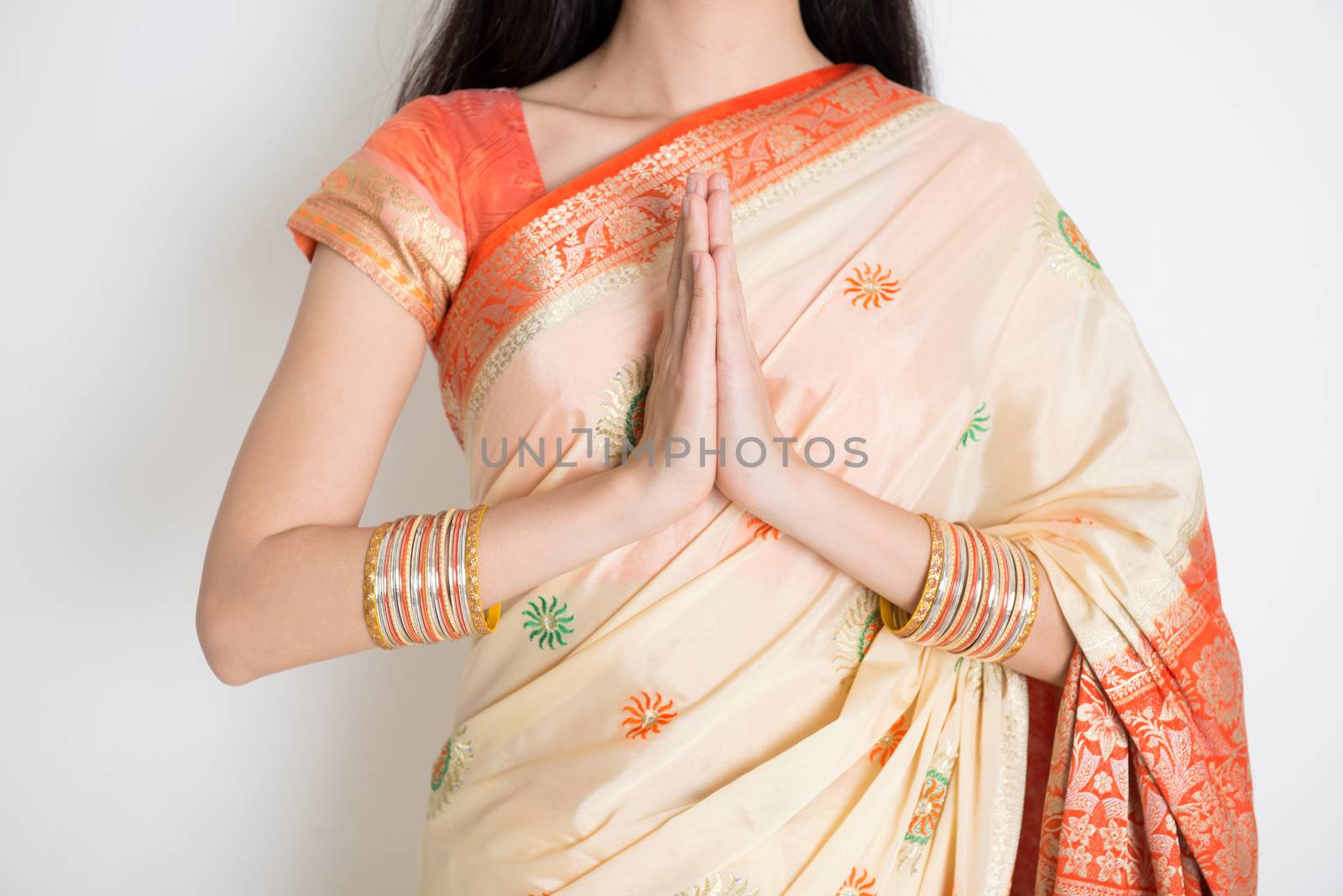 Fair skin Indian woman in traditional sari dress showing welcoming gesture, standing on plain background.