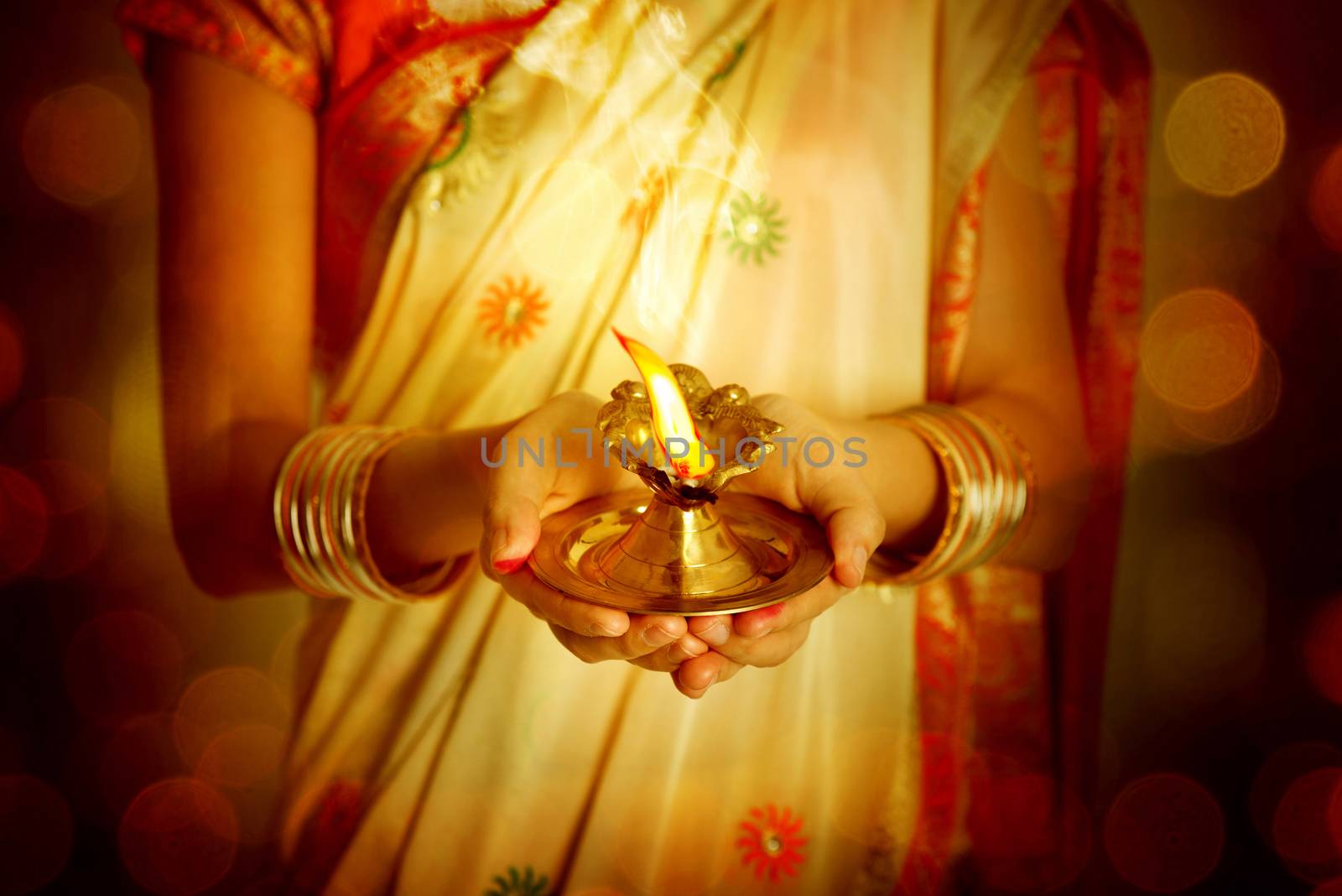 Close up Indian woman in traditional sari lighting oil lamp and celebrating Diwali or deepavali, fesitval of lights at temple. Female hands holding oil lamp.