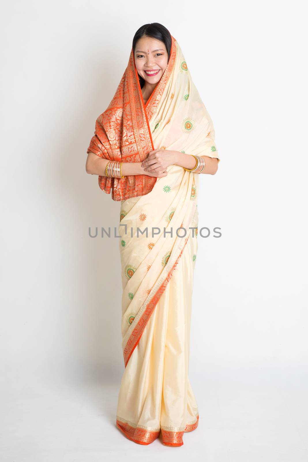 Portrait of young mixed race Indian Chinese woman in traditional sari dress smiling and looking at camera, full length on plain background.
