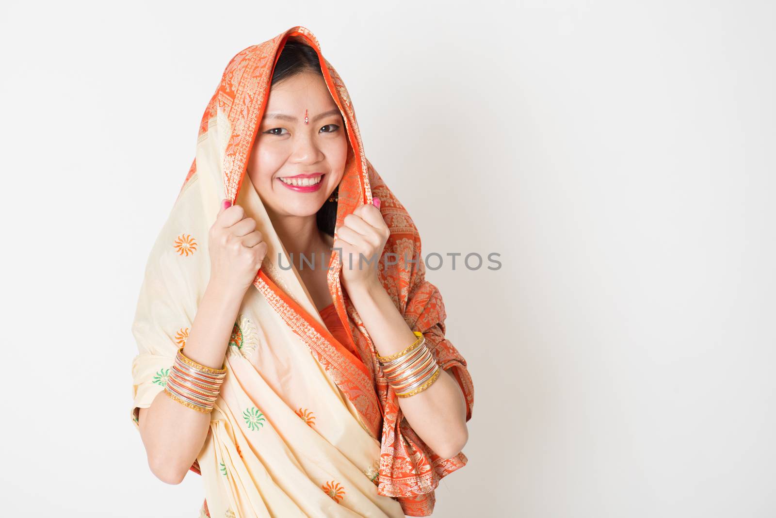 Portrait of young mixed race Indian Chinese woman in traditional sari dress smiling and looking at camera, with plain background.