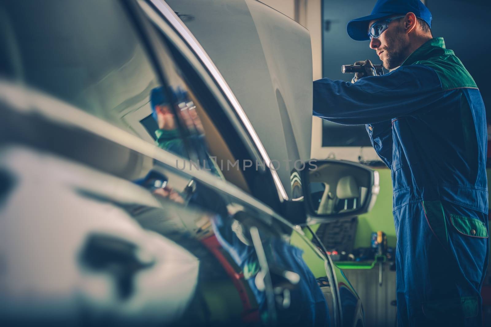 Car Mechanic Examining Vehicle Under the Hood. Caucasian Car Mechanic with Pro Flashlight at Work