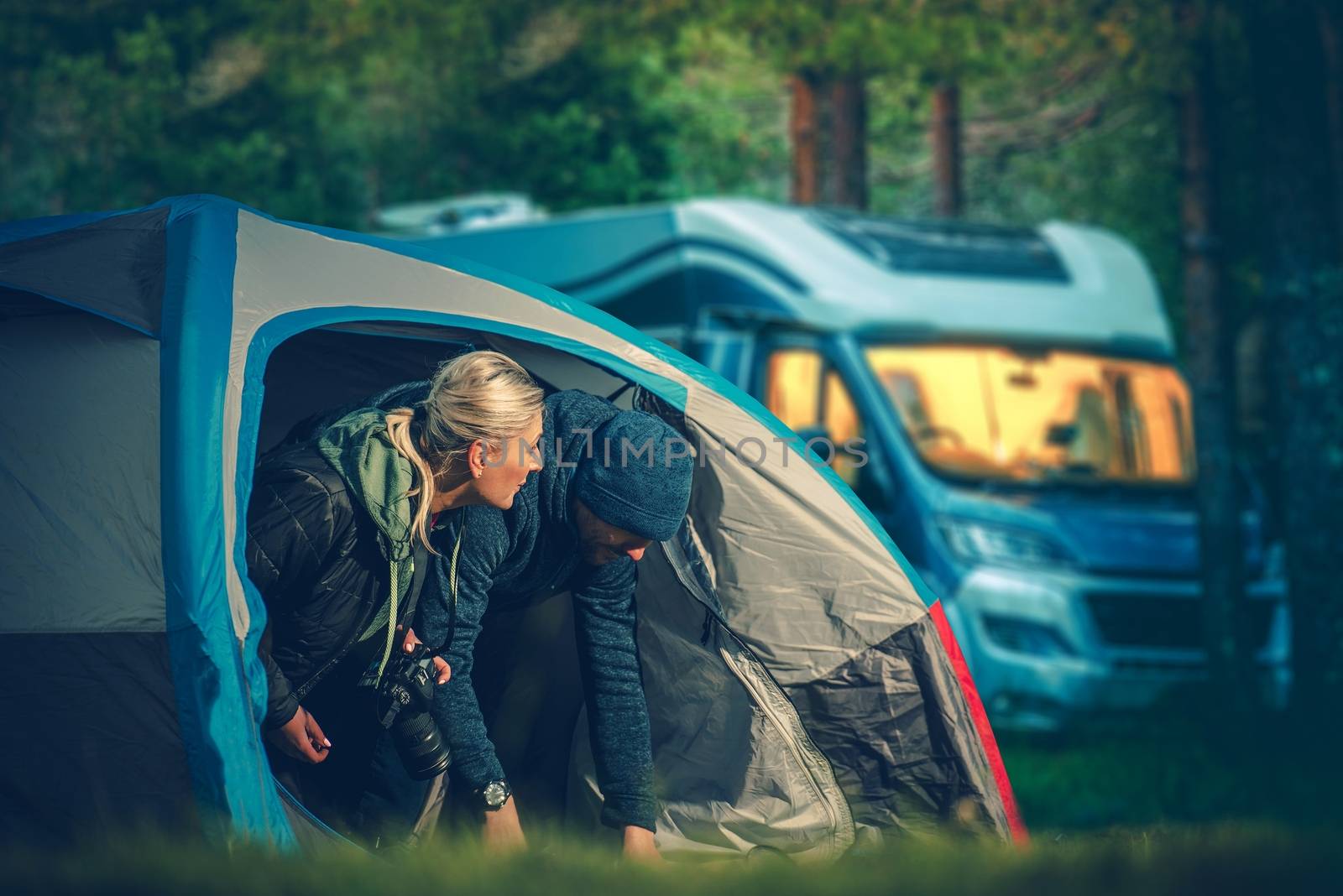 Couples Tent Camping. Men and Woman in Their 30s Camping in the Small Tent with Motorhome in the Background.