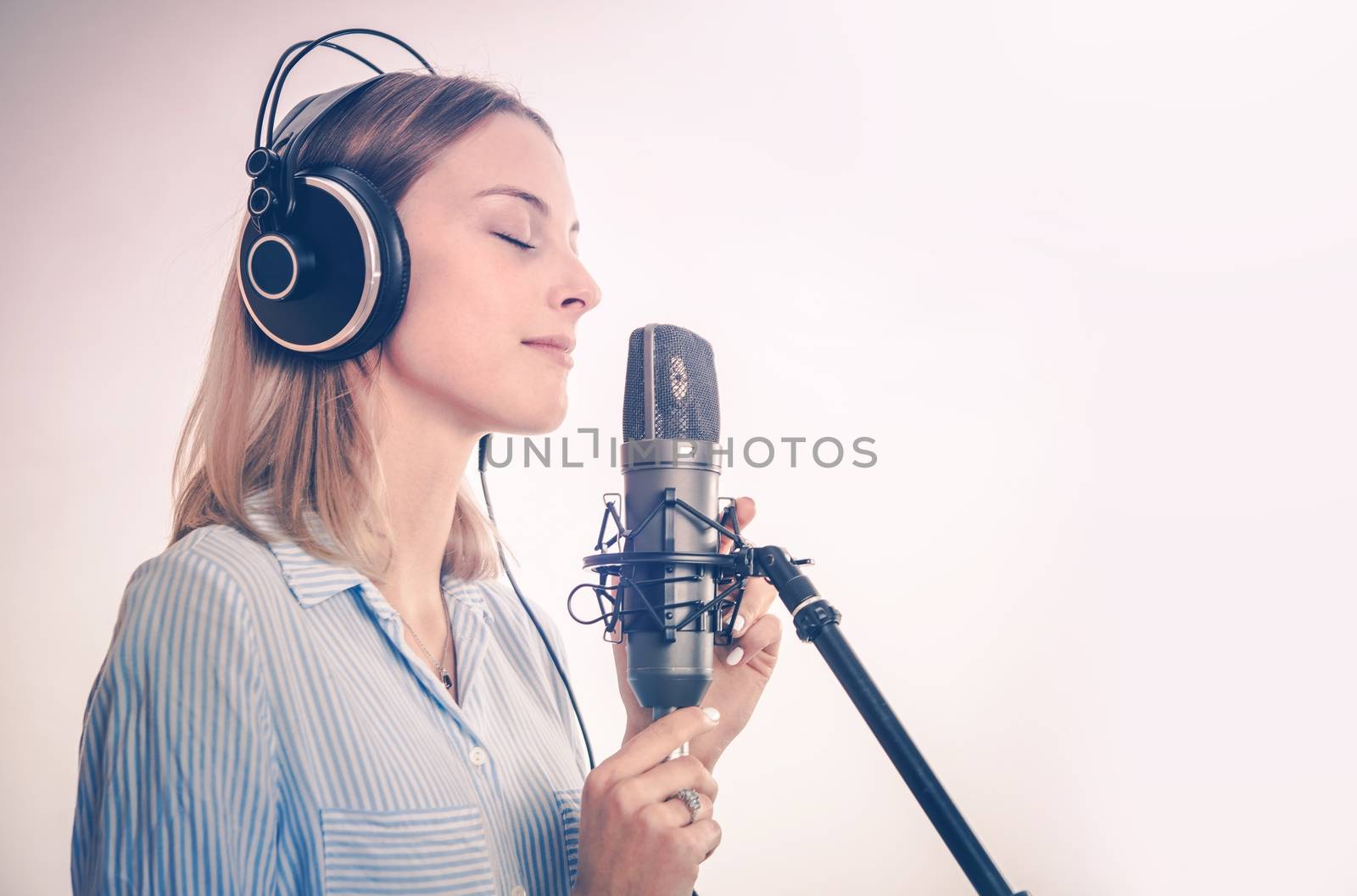 Female Vocal Recording. Young Woman with Microphone and Headphones in the Recording Studio.