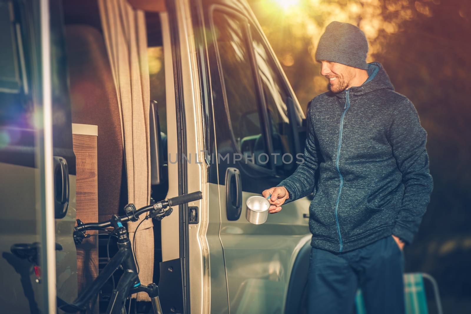 Satisfied Smiling Men with Small Cup of Coffee and His Camper Van Recreational Vehicle. RV and Mountain Bike Concept. Having Fun on the Camping. 