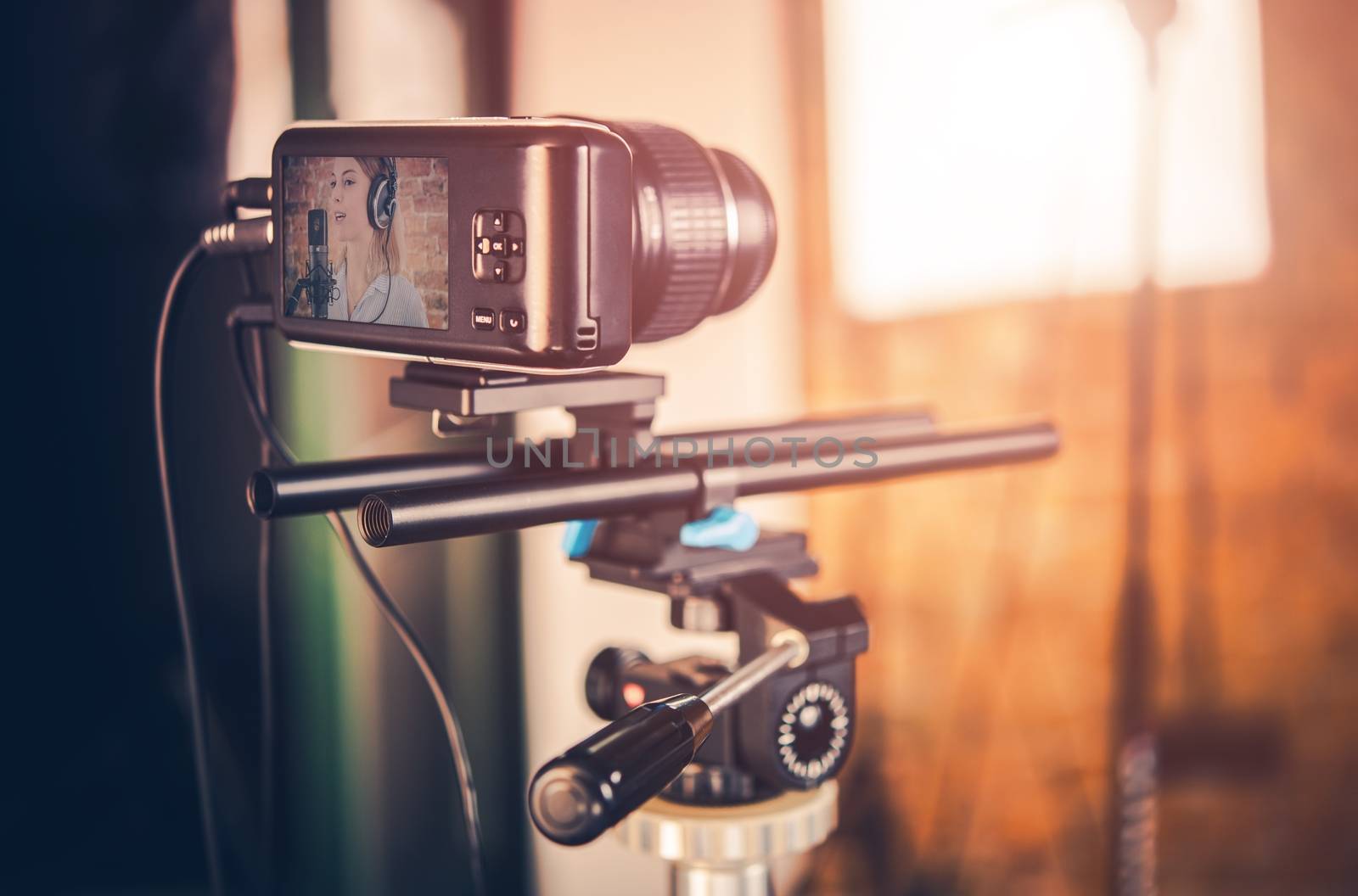 Modern Compact Video Equipment in Action. Small Video Camera on Tripod. Girl Singing to Microphone on the Camera Display.