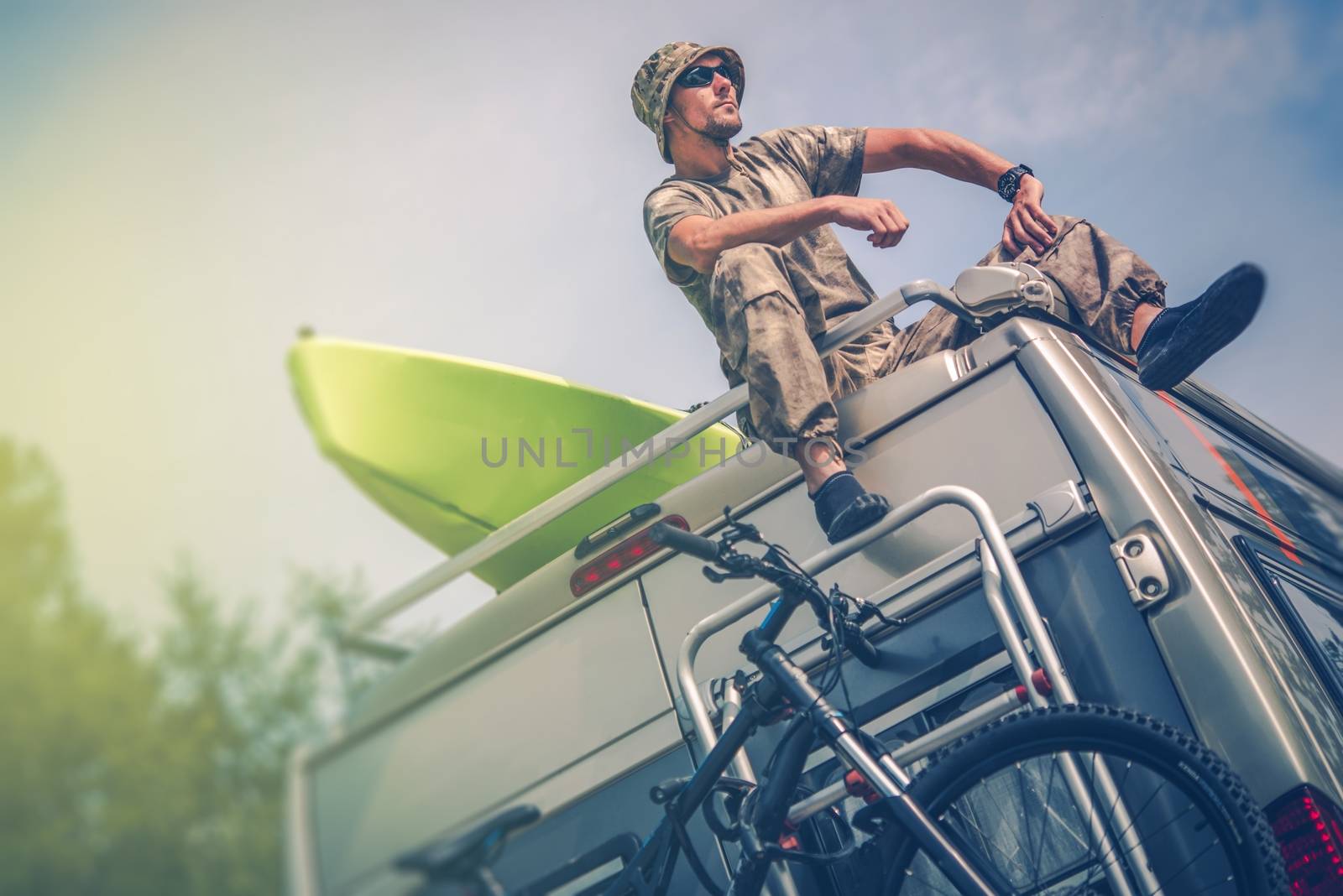 The Ultimate Outdoor Man. Caucasian Men Relaxing While Seating on the Roof of His RV Motorhome. RV Adventures with Bike and Kayak.