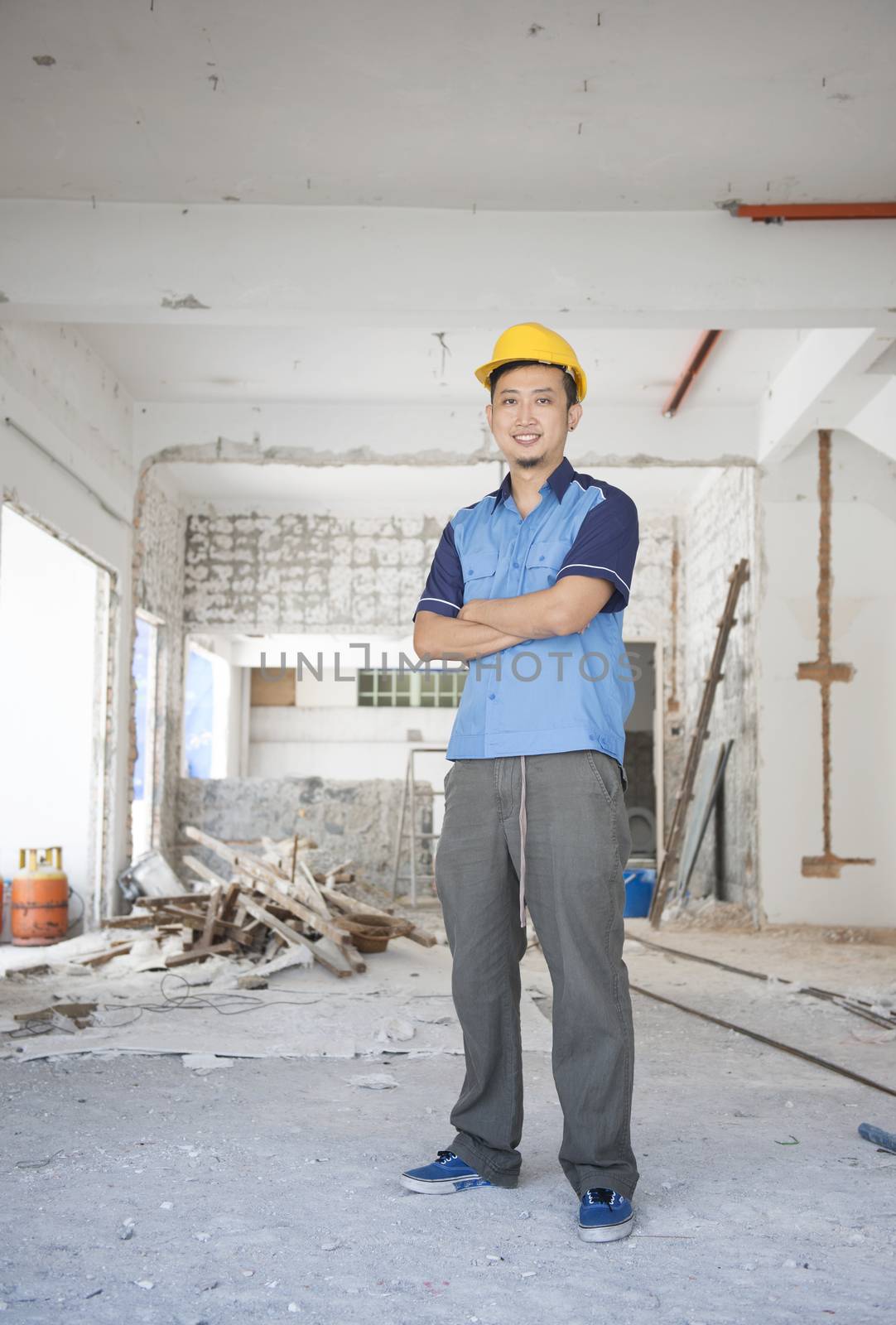 Asian construction worker with hardhat standing at site. 