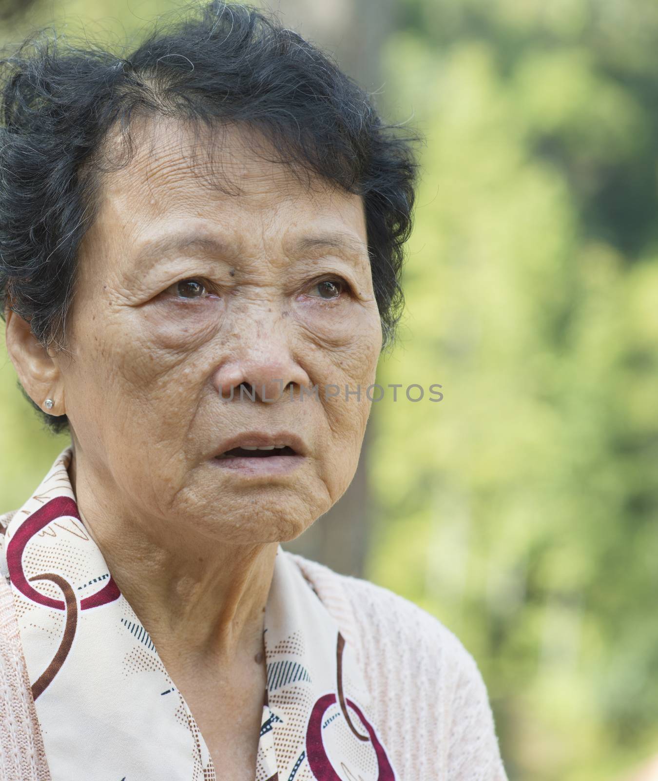 Portrait of worried Asian senior adult woman at outdoor garden park in the morning.