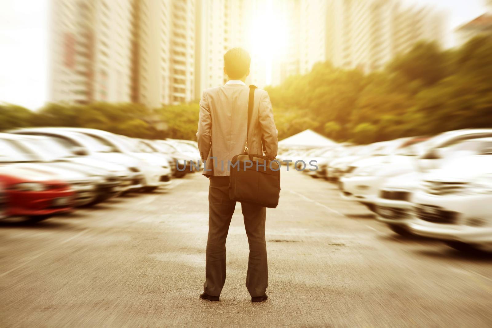 Rear view businessman standing at open car park, looking away with beautiful sunlight.