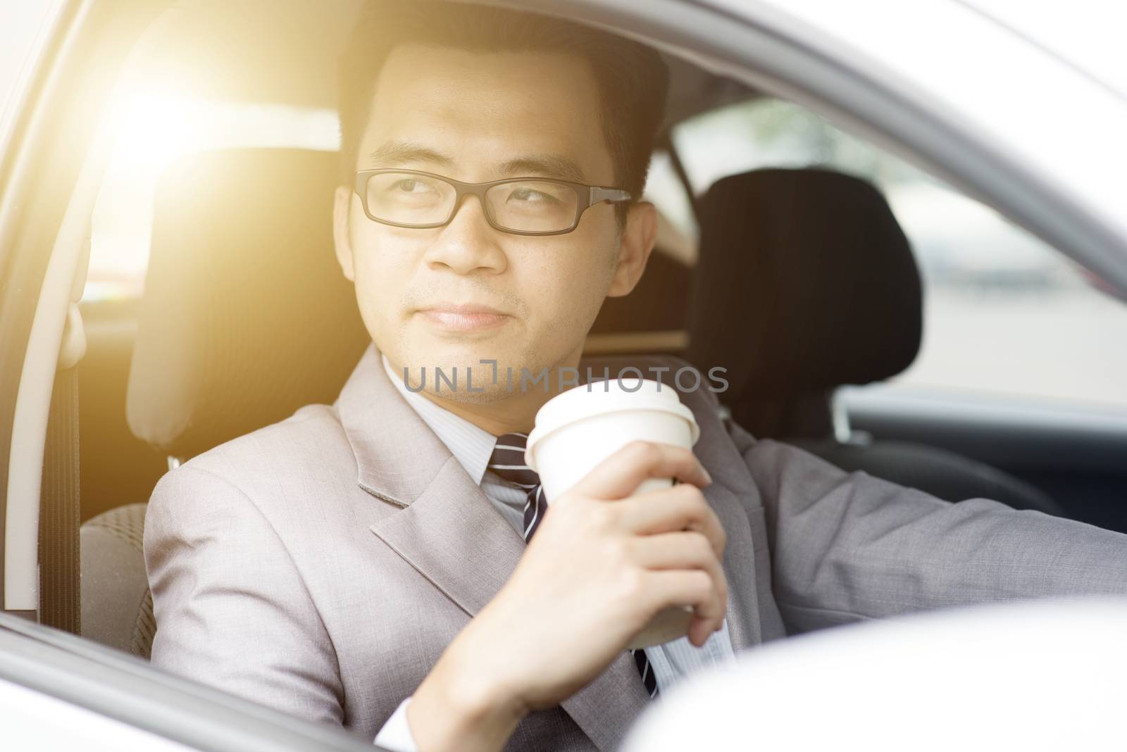 Asian business man drinking coffee while driving the car, in a morning with beautiful sunlight.