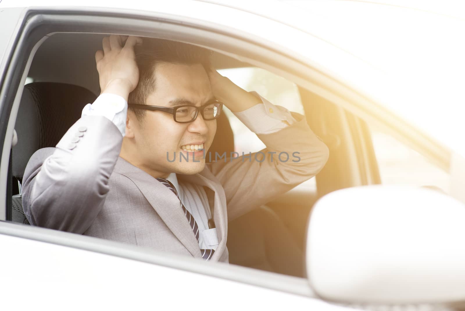Portrait displeased angry pissed off aggressive Asian business man driving car, shouting at someone in traffic hands grabbing hair. Emotional intelligence concept. Negative human expression.