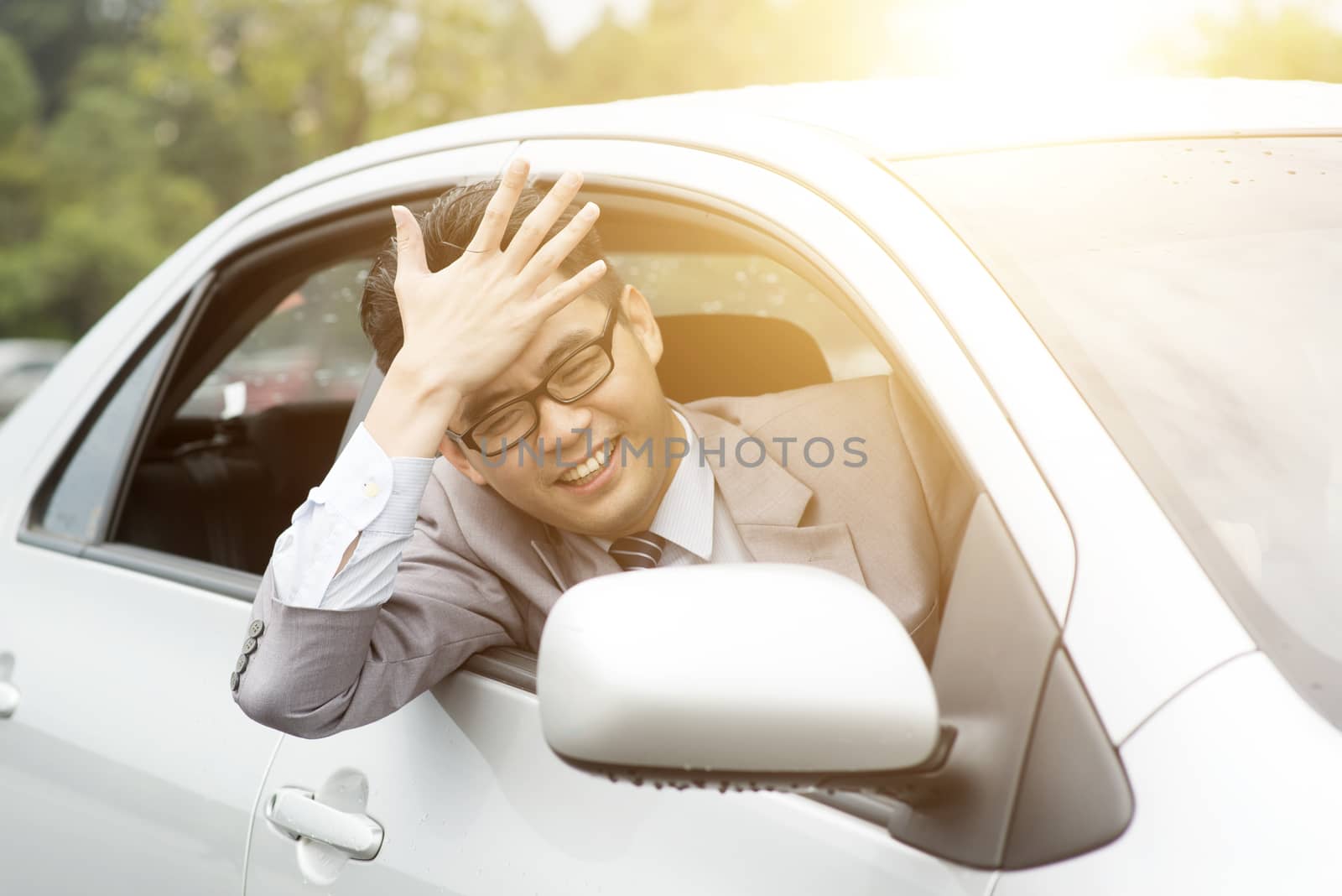 Portrait of pissed off  Asian business man driving car, hand banging his head in traffic jam. Negative human expression.