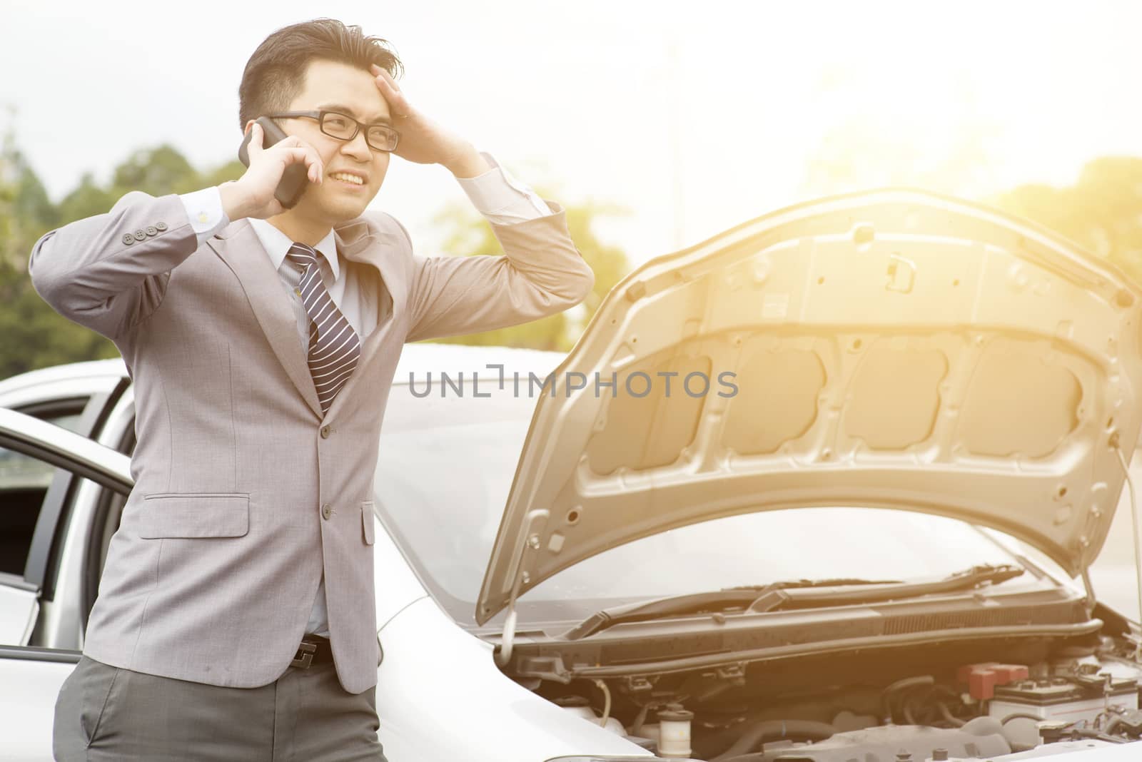 Asian business man standing by the Broken Down car and calling smart phone for help.