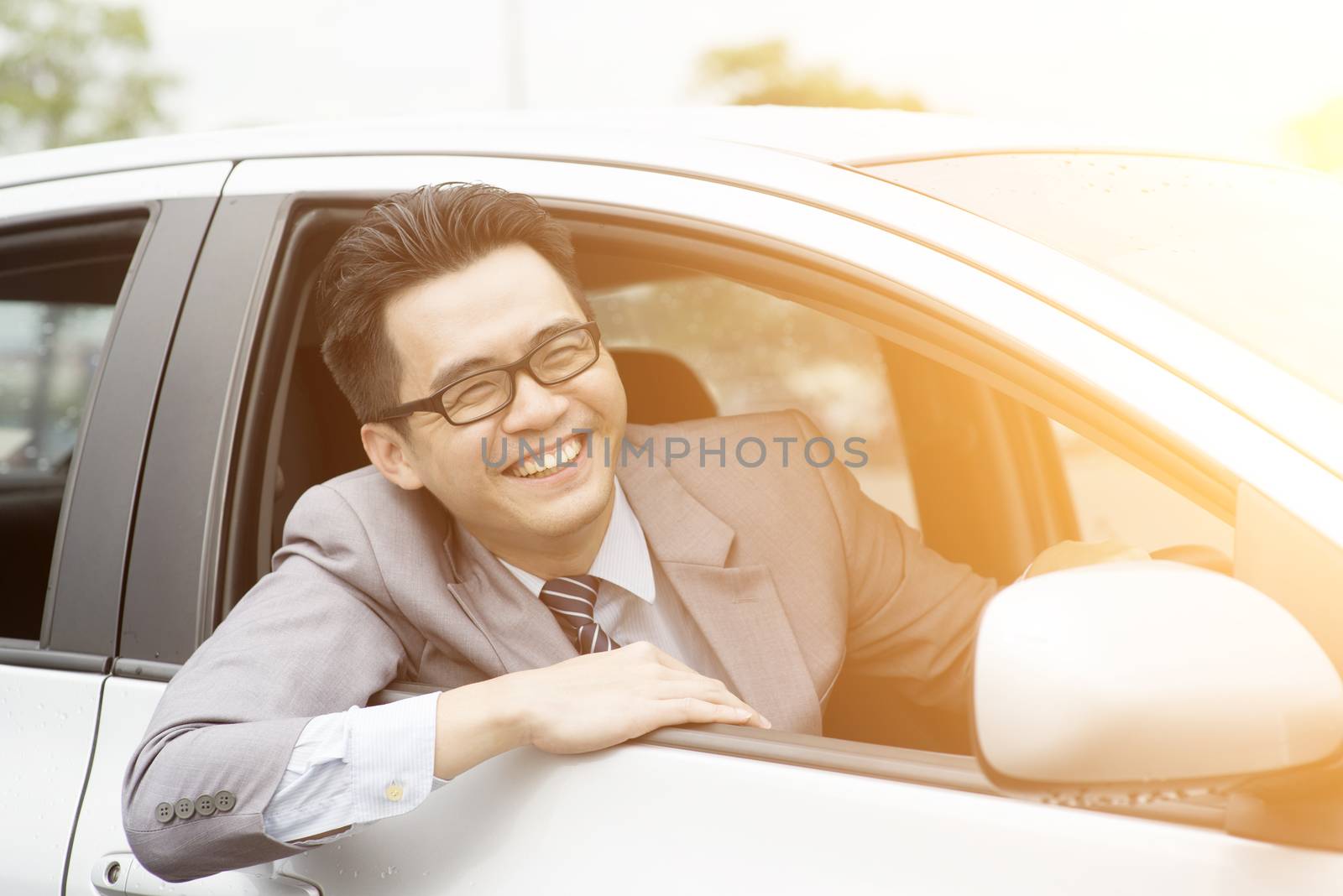 Happy Asian driver sitting in his car and smiling.