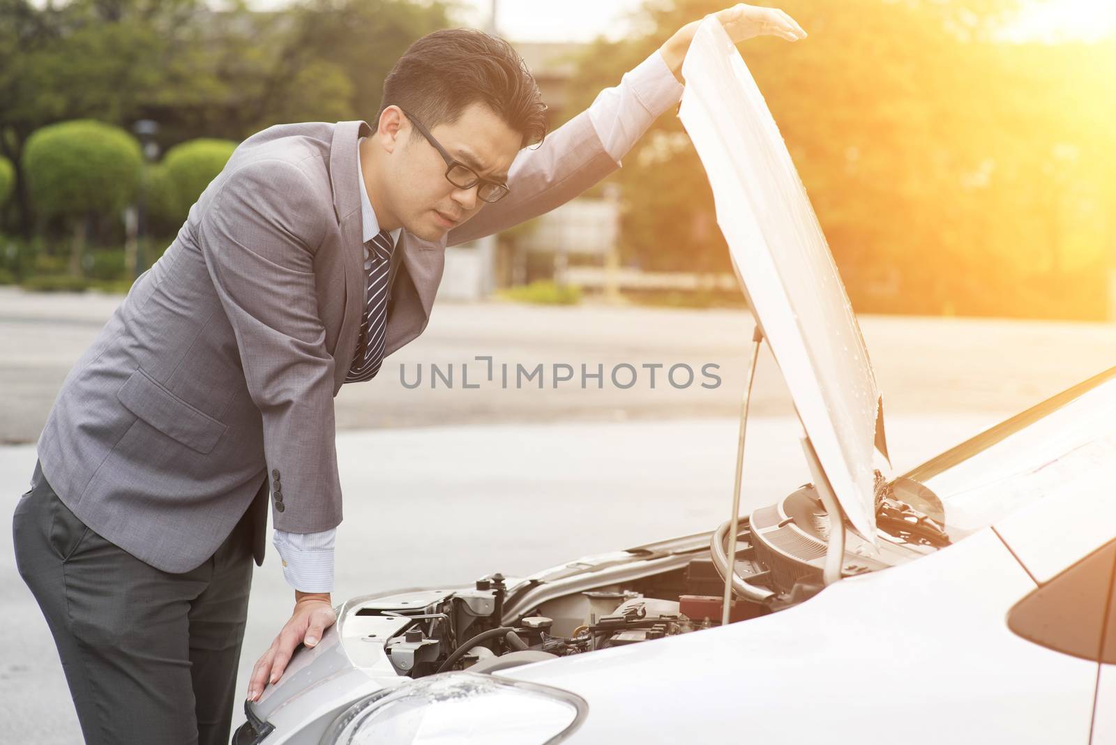 Young Asian business man looking under the hood of breakdown car.