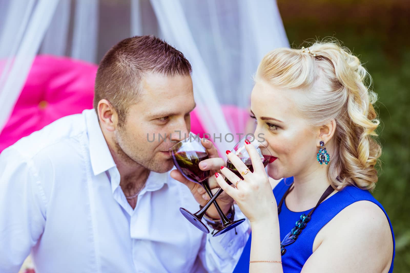 Man and woman sitting on the bed in the lawn and drinking wine from glasses and look at each other in Lviv, Ukraine.