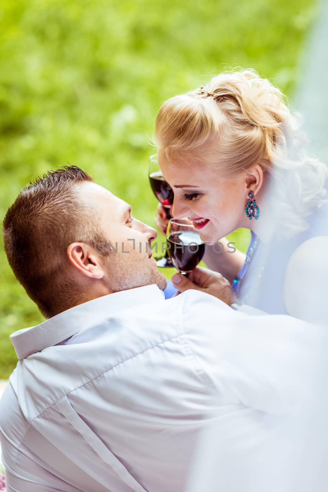 Man and woman sitting on the bed in the lawn and holding a glasses of wine and look at each other in Lviv, Ukraine.