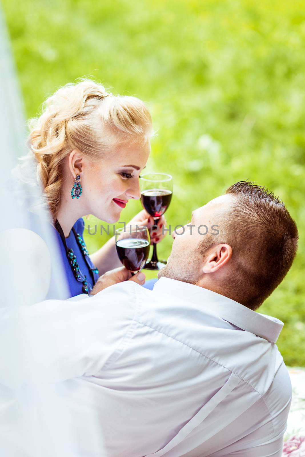 Man and woman sitting on the bed in the lawn and holding a glasses of wine and look at each other in Lviv, Ukraine.