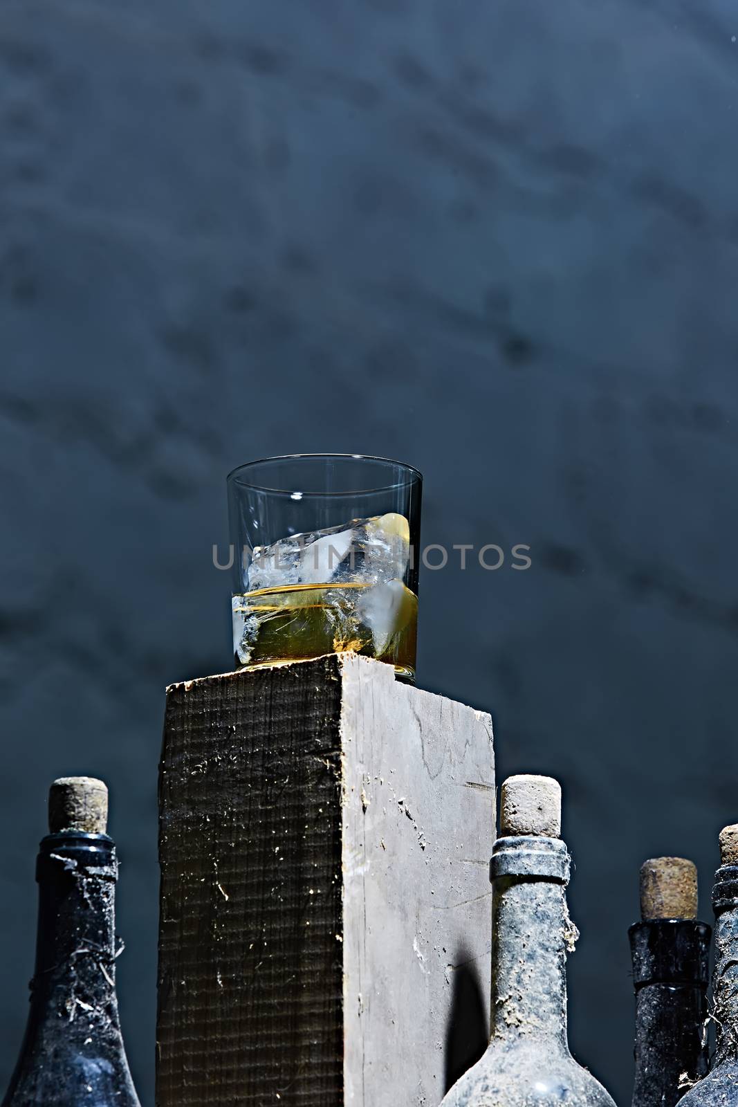 A glass of whiskey with ice on old wooden bar around the old bottles. Shallow dof