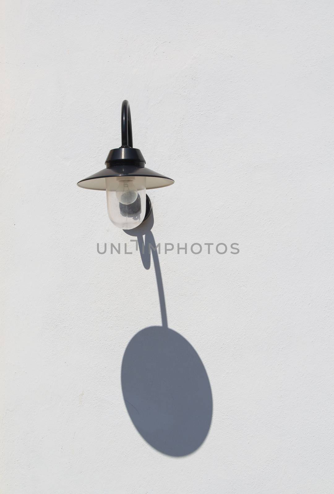 White facade of a building with a stylish wall street lamp. Shadow of a lamp on the wall.