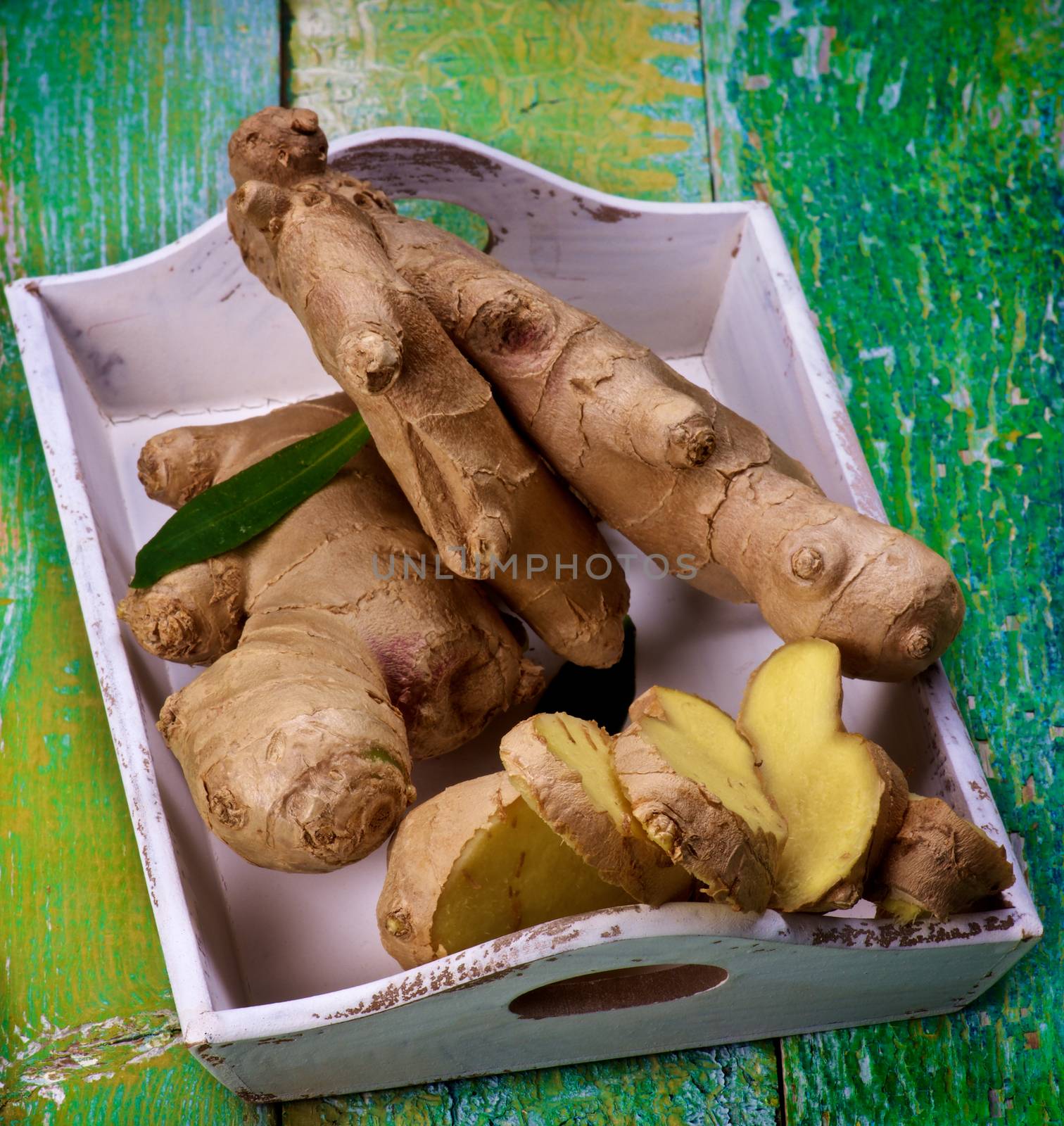 Arrangement of Fresh Raw Ginger Full Body and Slices in White Tray closeup on Cracked Wooden background