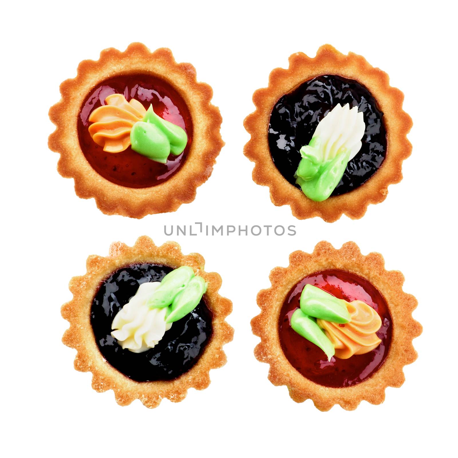 Arrangement of Delicious Little Tarts with Colored Butter Cream, Fruit Jam and Decoration closeup on White background. Top View