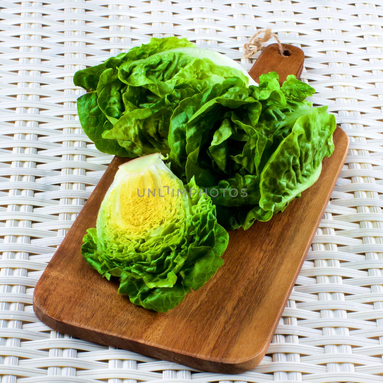 Fresh Crunchy Romaine Lettuce Full Head and Half on Wooden Cutting Board closeup on Wicker background