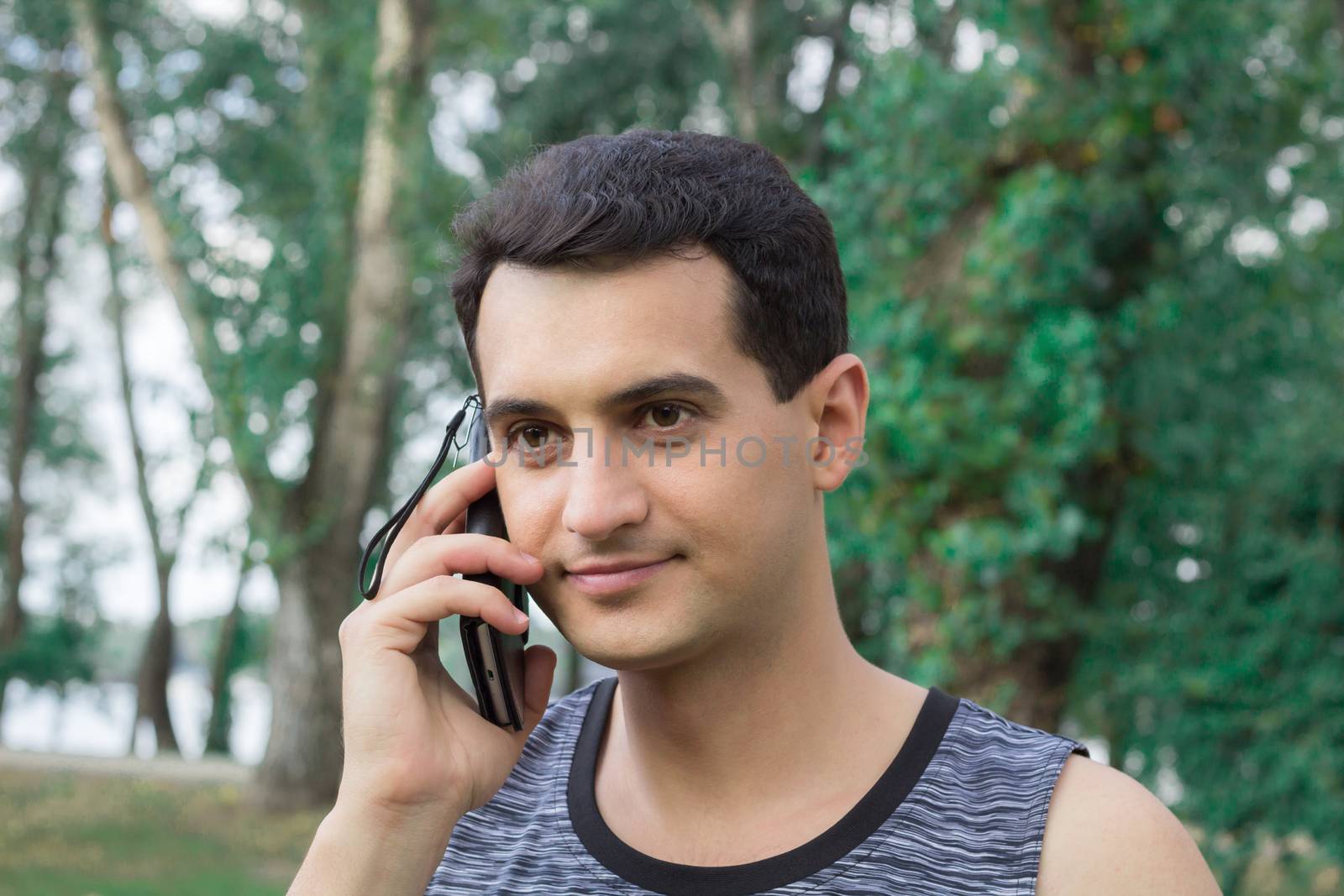Young fitness man talks by mobile phone during training workout outdoor