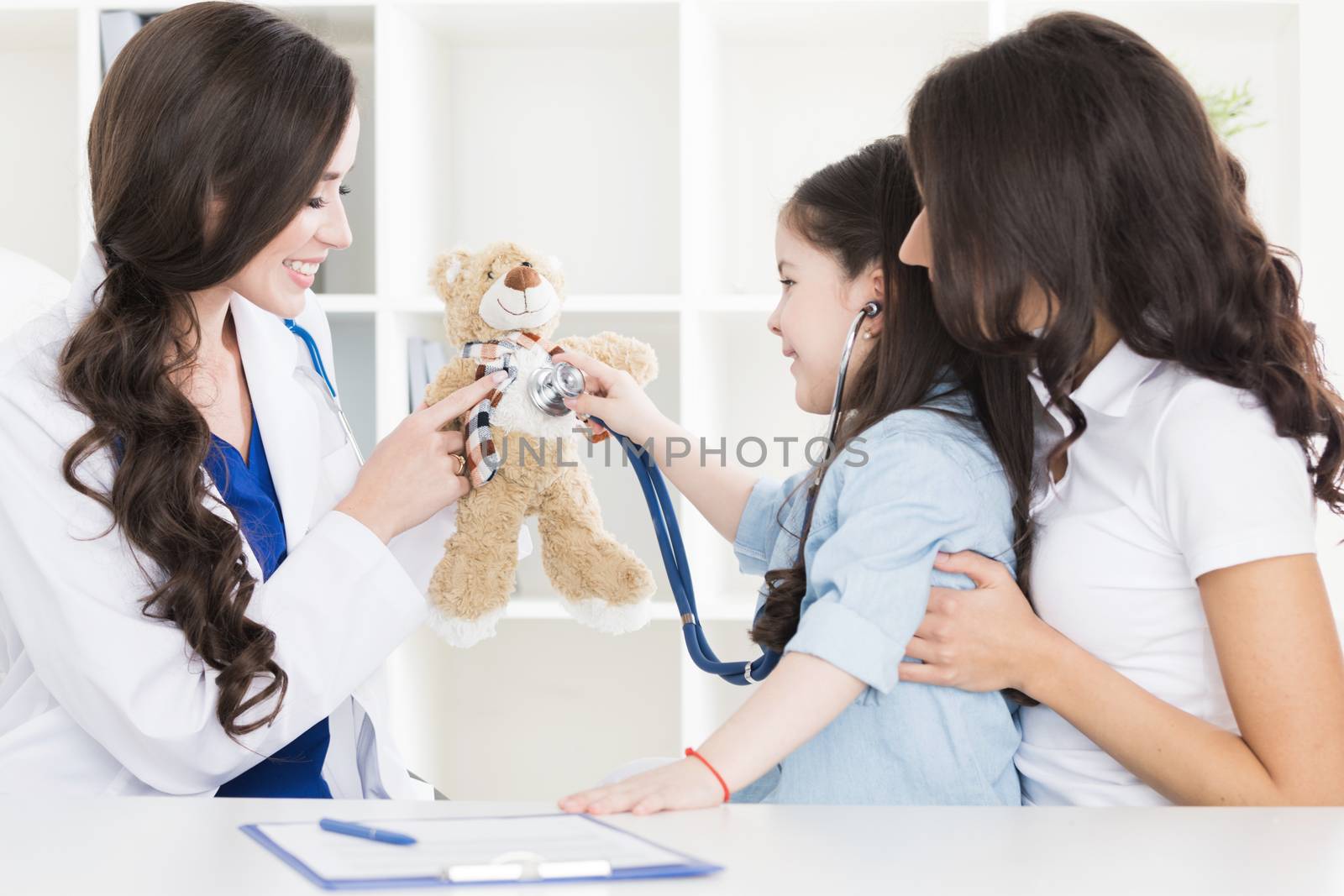 Pediatrist examinate heart beat of teddy bear of small girl