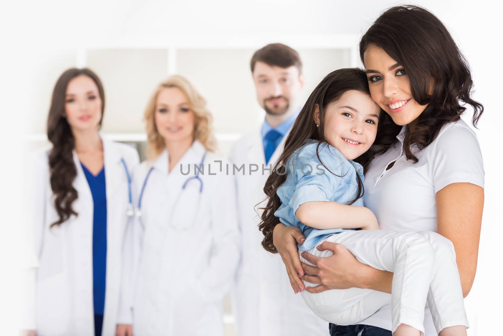 Young mother with daughter and droup of doctors on background in hospital