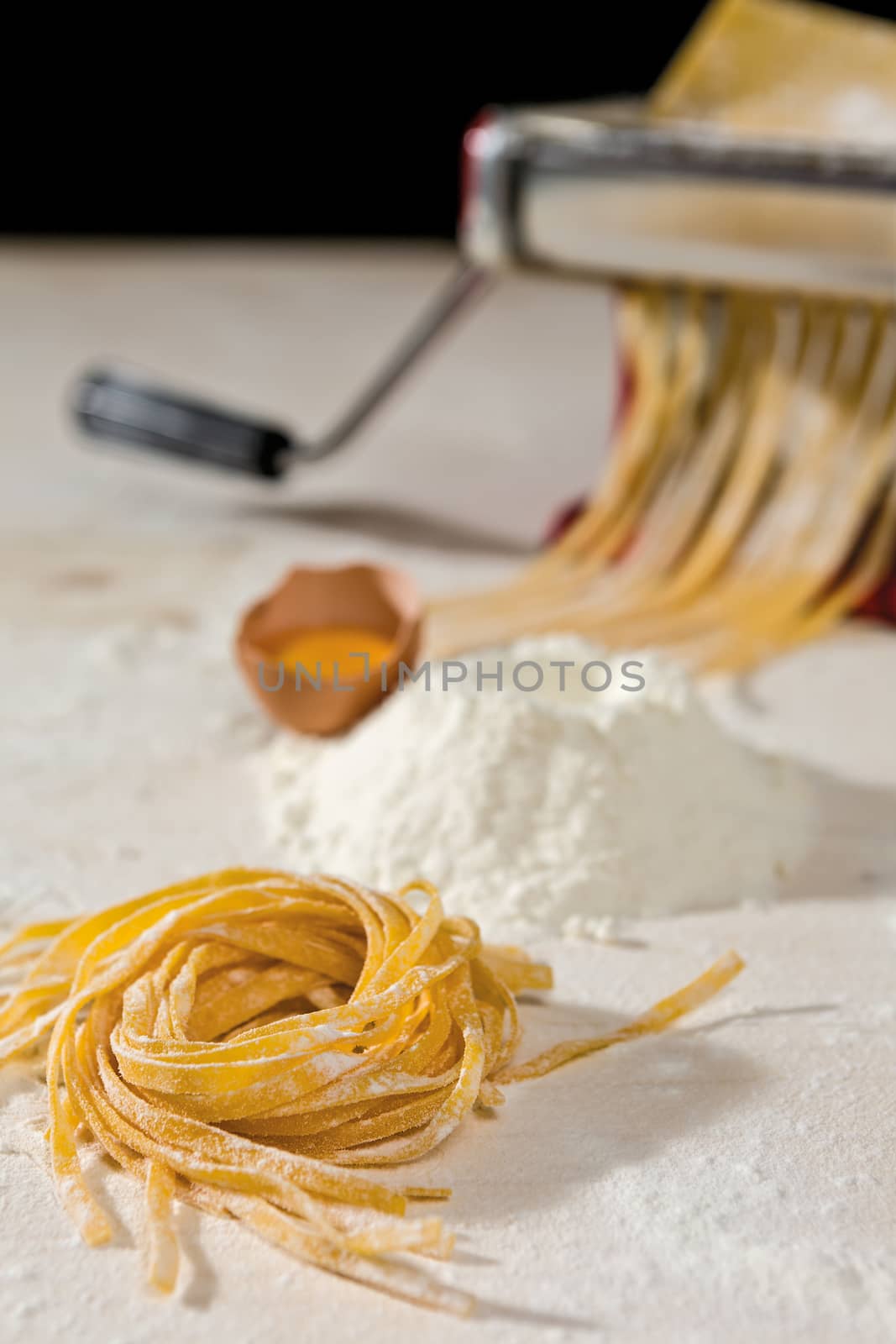 Tagliatelle pasta and its ingredients with machine pasta cutter on background