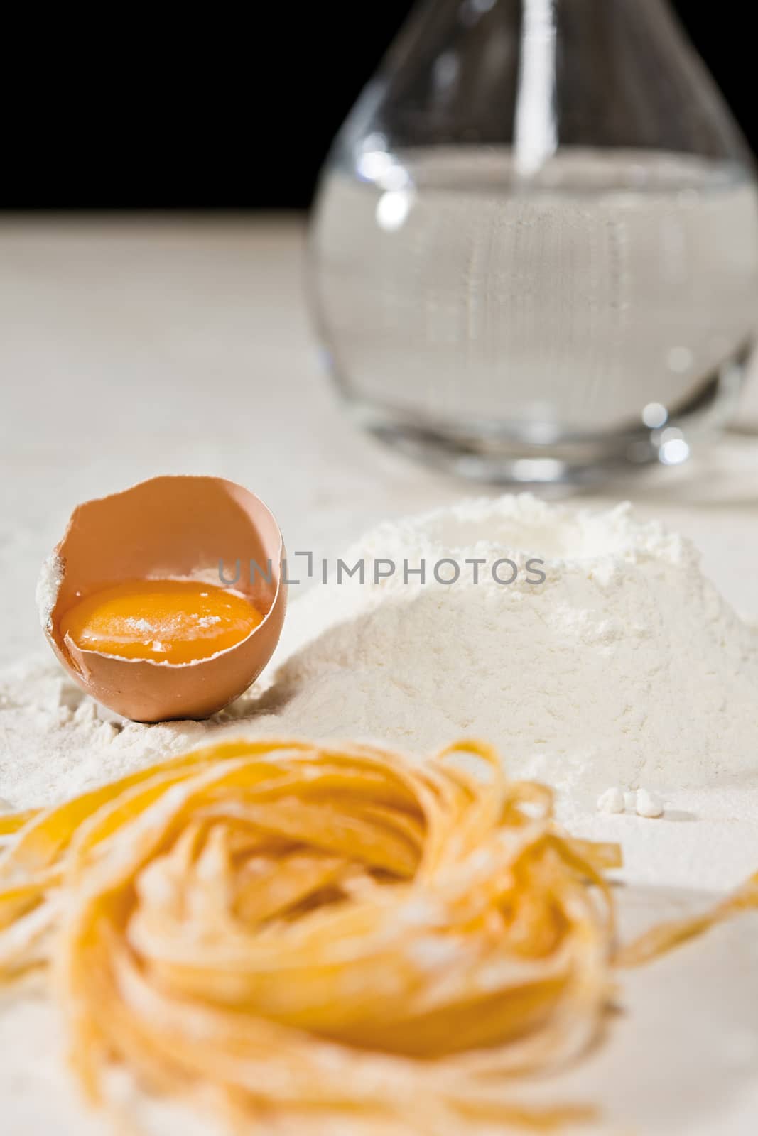 Closeup of Italian tagliatelle pasta and its ingredients with some water on background