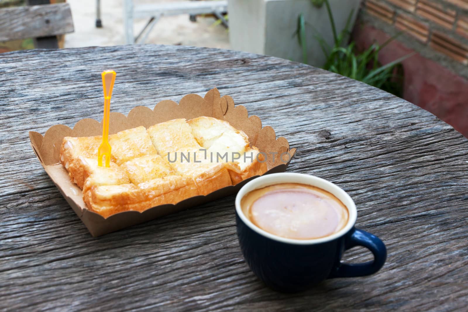 Toast with butter milk in paper tray and espresso on wood table