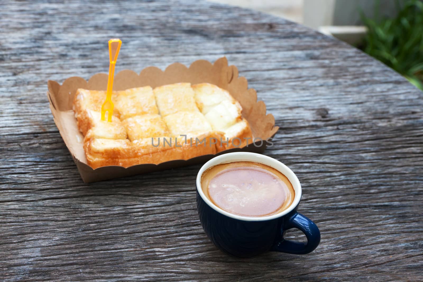 Toast with butter milk in paper tray and espresso on wood table