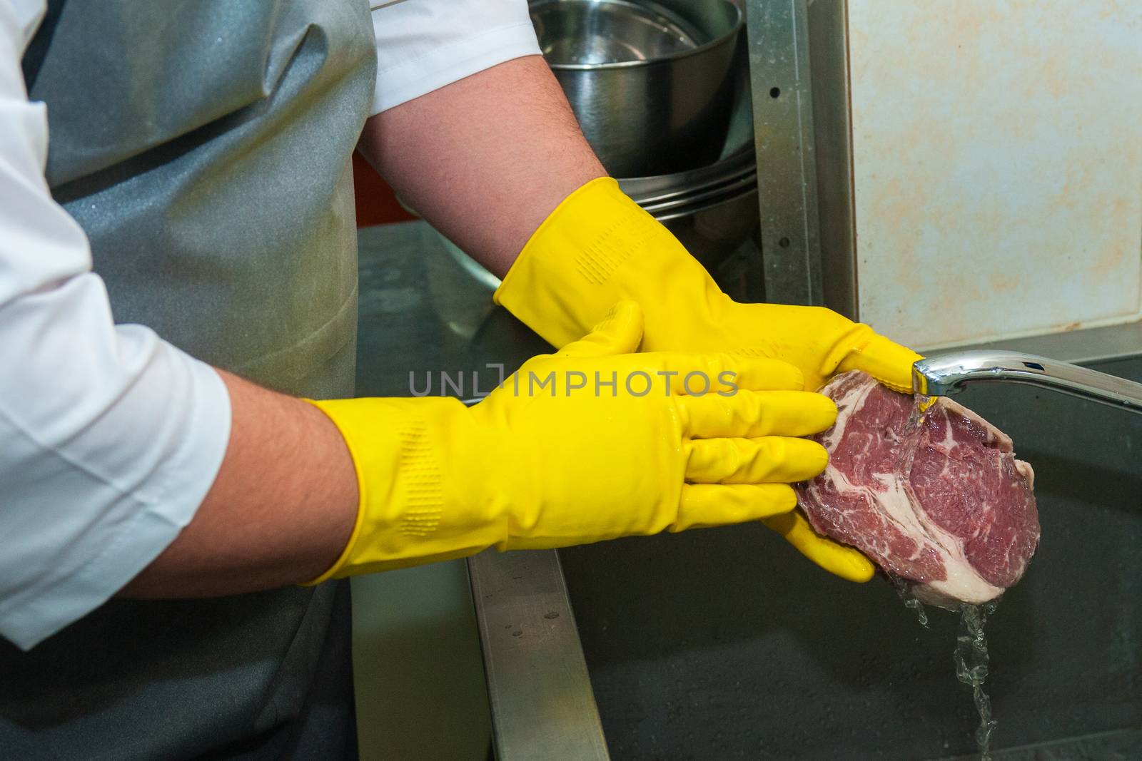 Hands in gloves washing and cleaning meat at the kitchen sink