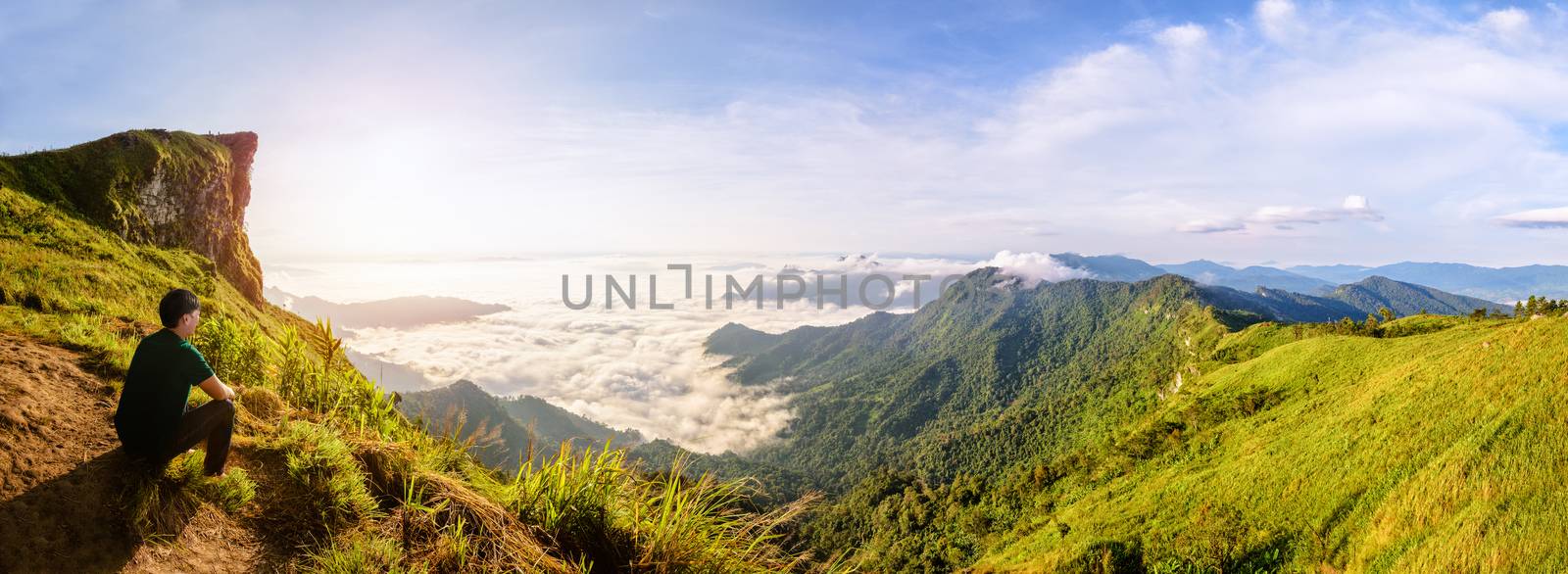Panorama beautiful landscape nature, Male tourist are watching the sunrise on peak mountain with sun cloud fog and bright sky in winter at Phu Chi Fa Forest Park, famous attraction of Chiang Rai Province, Thailand