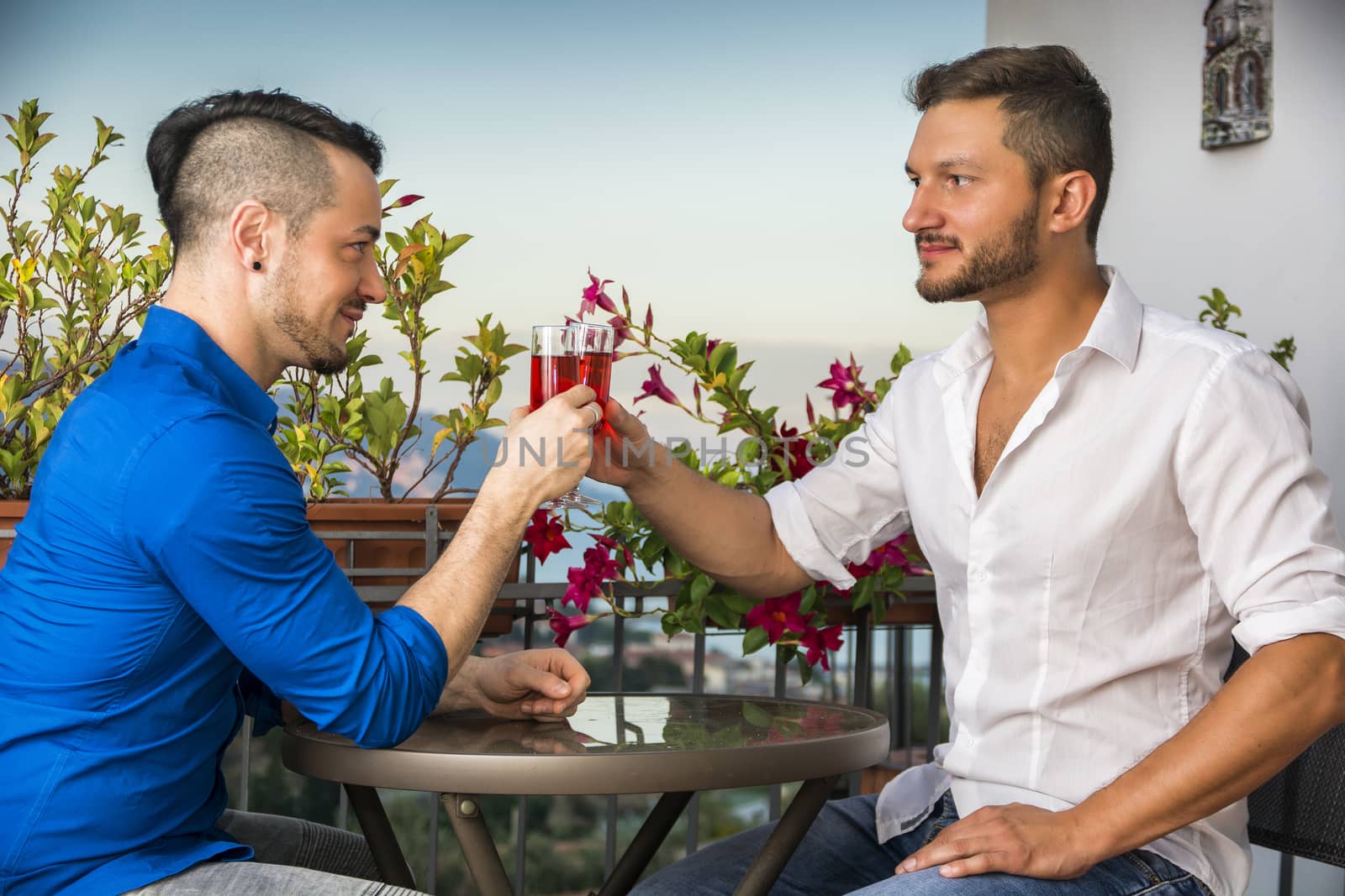 Two handsome young men sitting at the table with wine by artofphoto